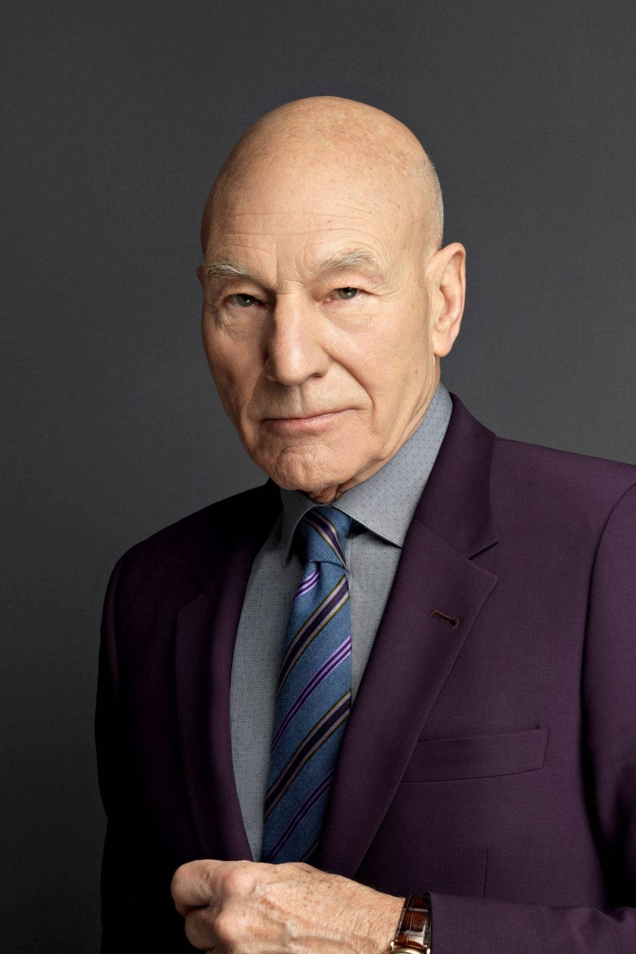 Celebrity 桌布 壁紙 — 一個光頭男子穿著紫色西裝和條紋領帶，在深灰色背景前擺出嚴肅的表情。