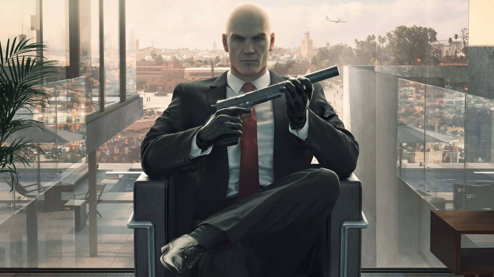 1920x1080 Hitman Absolution 桌布 壁紙 — 一個光頭男子穿著西裝，冷靜地坐在椅子上，手持一把消音手槍，身後透過玻璃窗可以看到城市景觀。