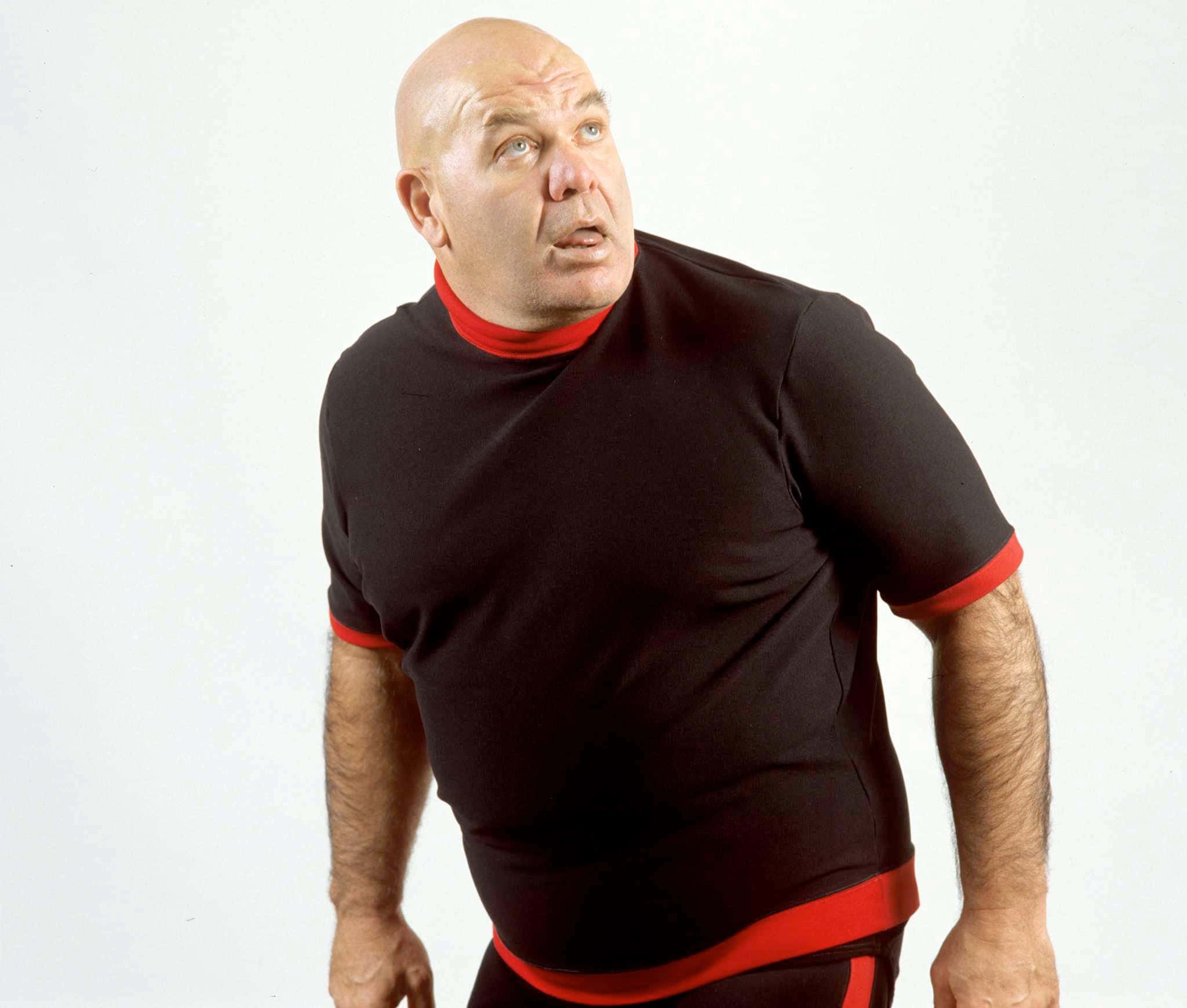 WWE 桌布 壁紙 — 一個光頭男子穿著黑色和紅色的摔角服，在純白色背景上帶著驚訝的表情向上看。