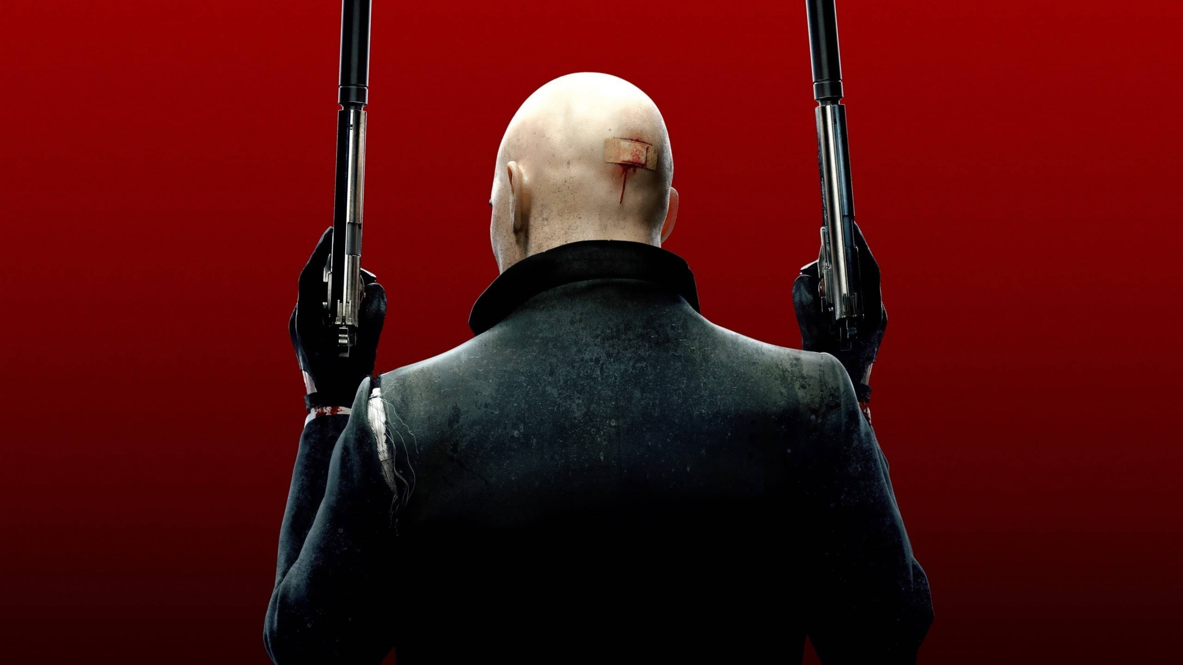 桌布 壁紙 — 一個光頭男子穿著黑色西裝，舉起兩把手槍，背景是鮮豔的紅色，頭部有一道明顯的疤痕。