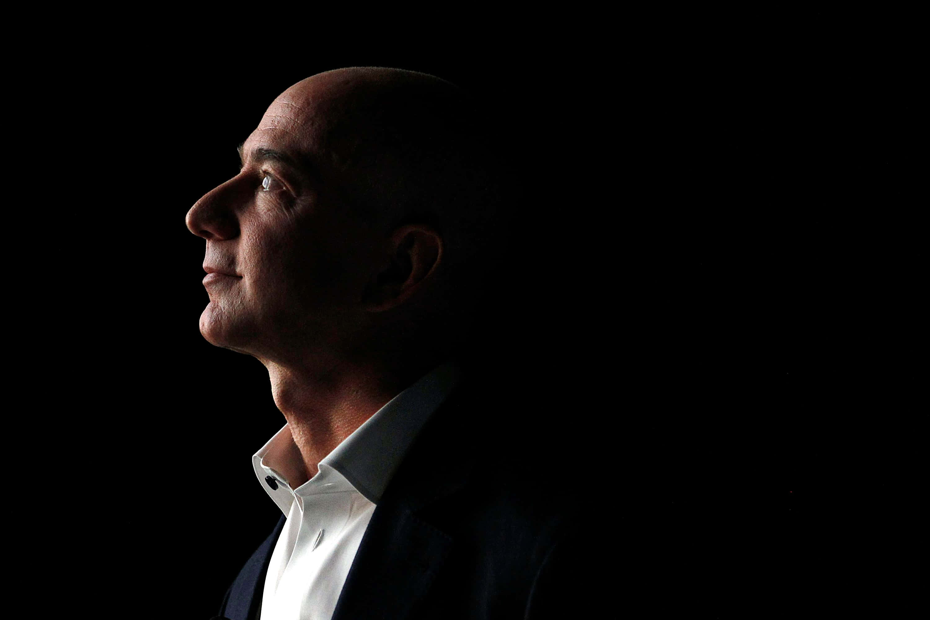 Jeff Bezos 桌布 壁紙 — 一個光頭男子身穿深色西裝和白色襯衫，在黑色背景前以側面輪廓呈現，側光凸顯其面部特徵。
