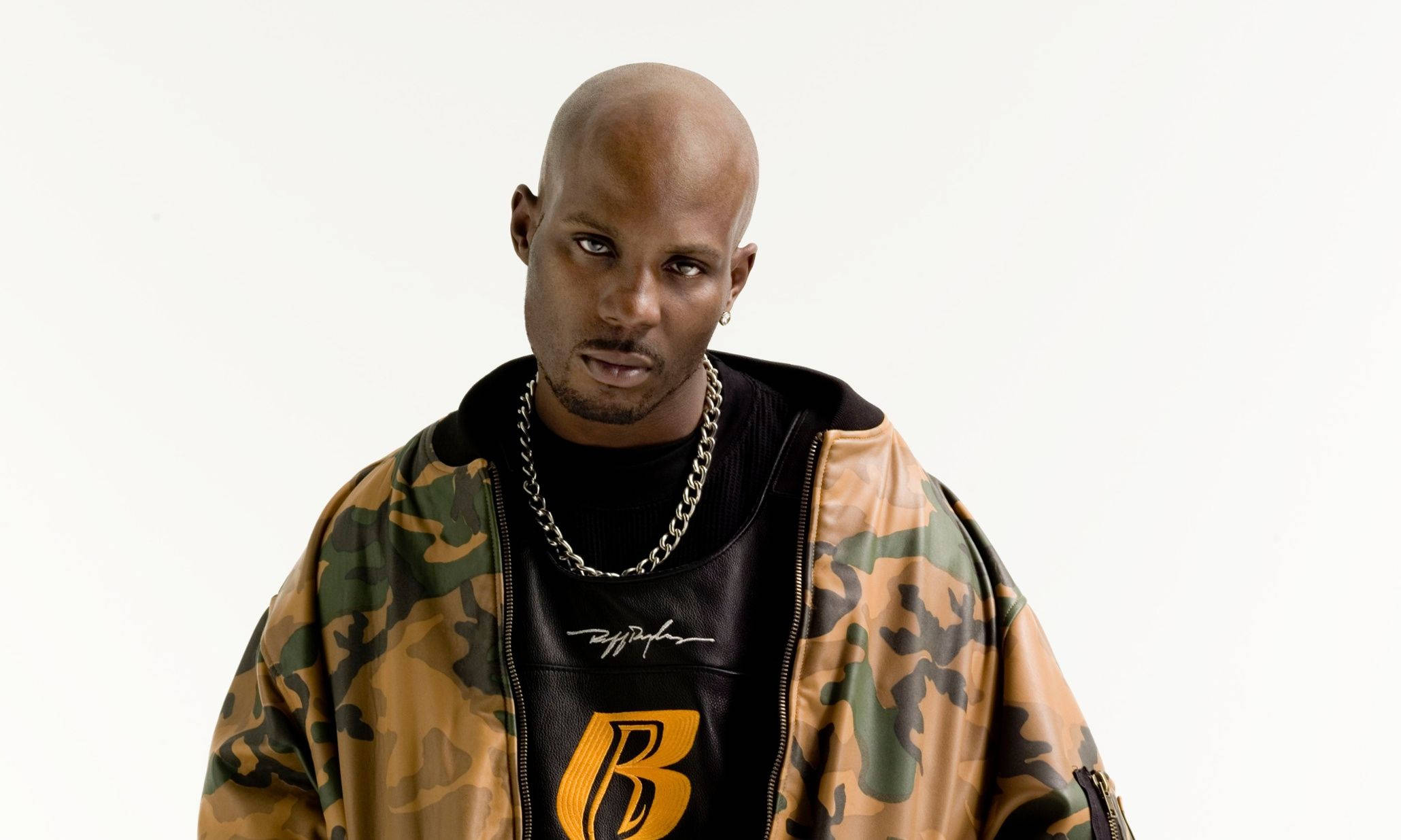 Dmx 桌布 壁紙 — 一個光頭男子身穿迷彩外套和鏈條項鍊，在純白背景下強烈凝視。