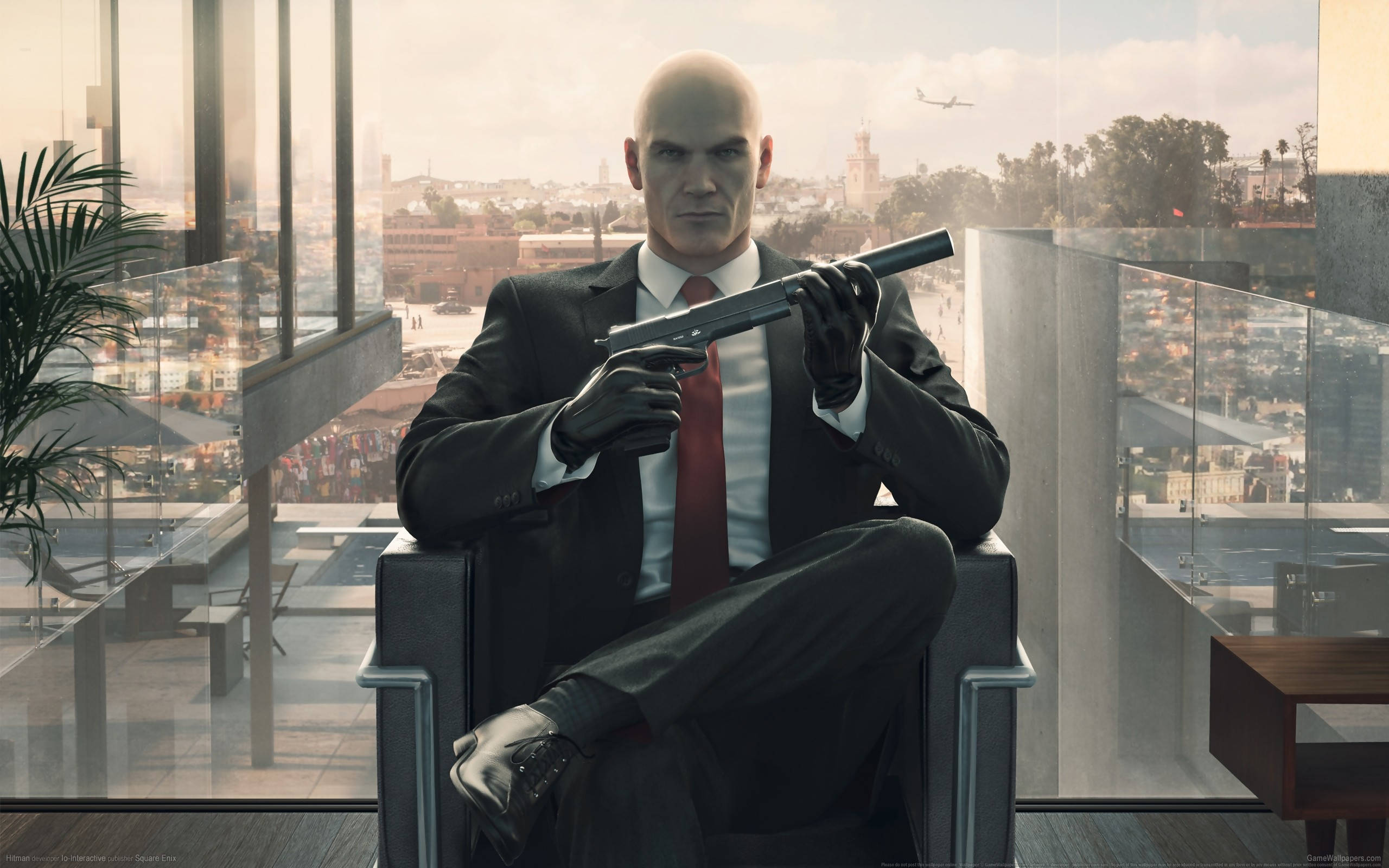 hitman absolution HD 桌布 壁紙 — 一個光頭男子身穿黑色西裝和紅色領帶，平靜地坐在現代玻璃辦公椅上，手持一把消音手槍，背後窗戶可見城市天際線。