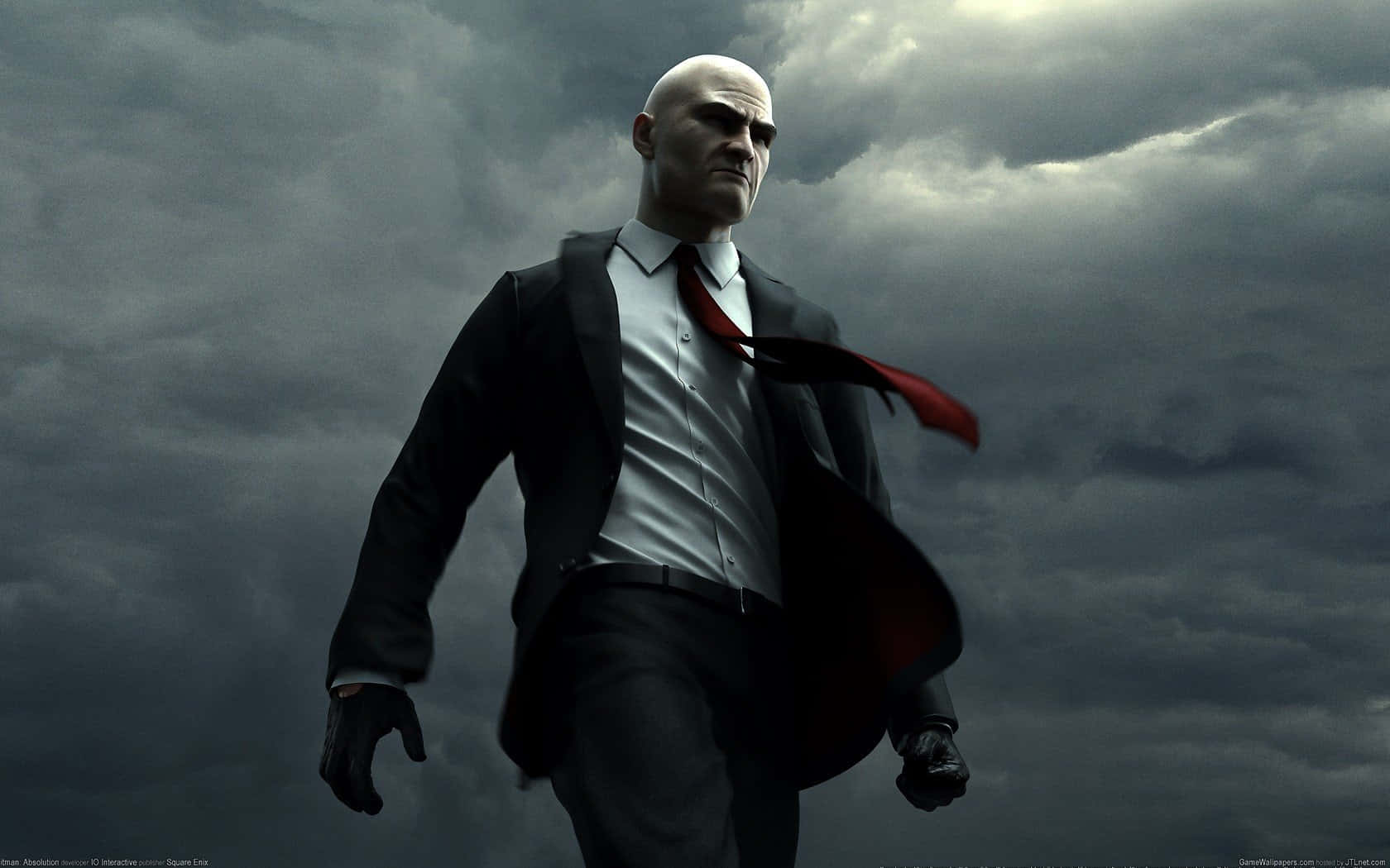 1080p Hitman Absolution 桌布 壁紙 — 一個光頭男子身穿黑色西裝和紅色領帶，在暴風雨的灰色天空下帶著強烈的表情大步向前。