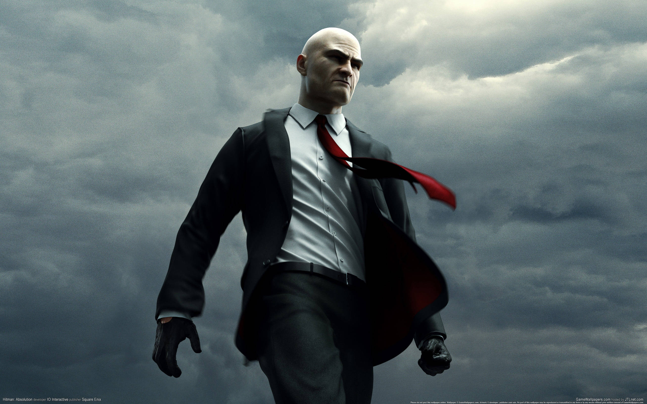 hitman absolution HD 桌布 壁紙 — 一個光頭男子身穿黑色西裝和紅色領帶，在暴風雨般的灰色天空下帶著強烈的表情大步向前。