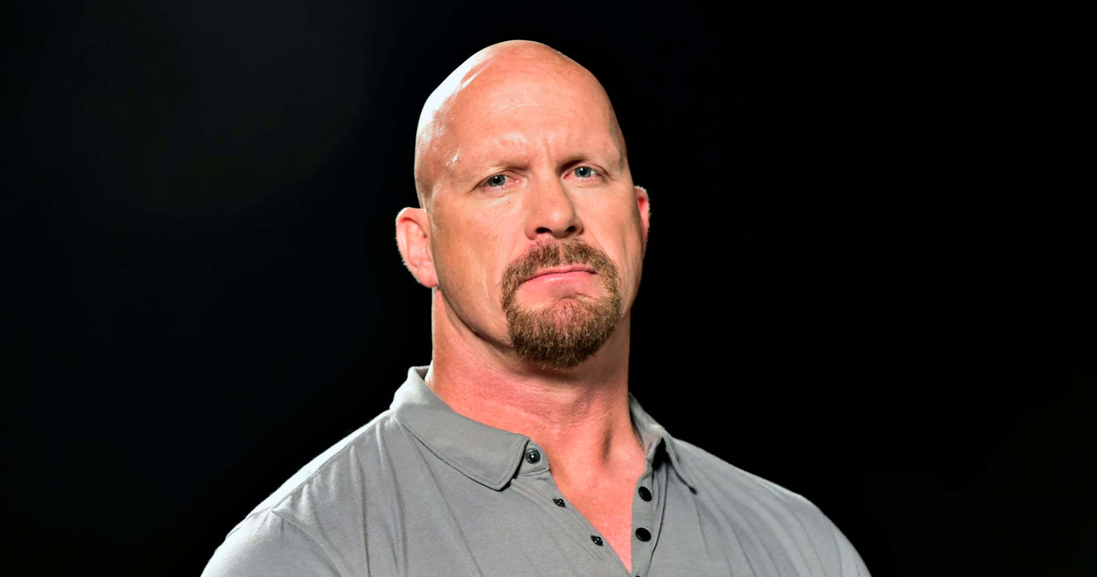 WWE 桌布 壁紙 — 一個光頭留山羊鬍的男人穿著灰色鈕扣襯衫，在黑色背景前專注地凝視。