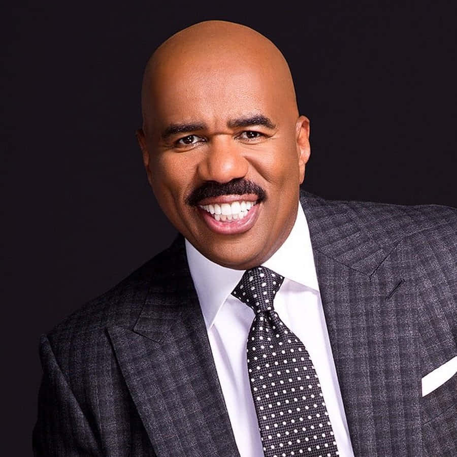 steve harvey 桌布 壁紙 — 一個光頭留鬍鬚的男人，身穿深色西裝和波點領帶，在黑色背景前燦爛地微笑。