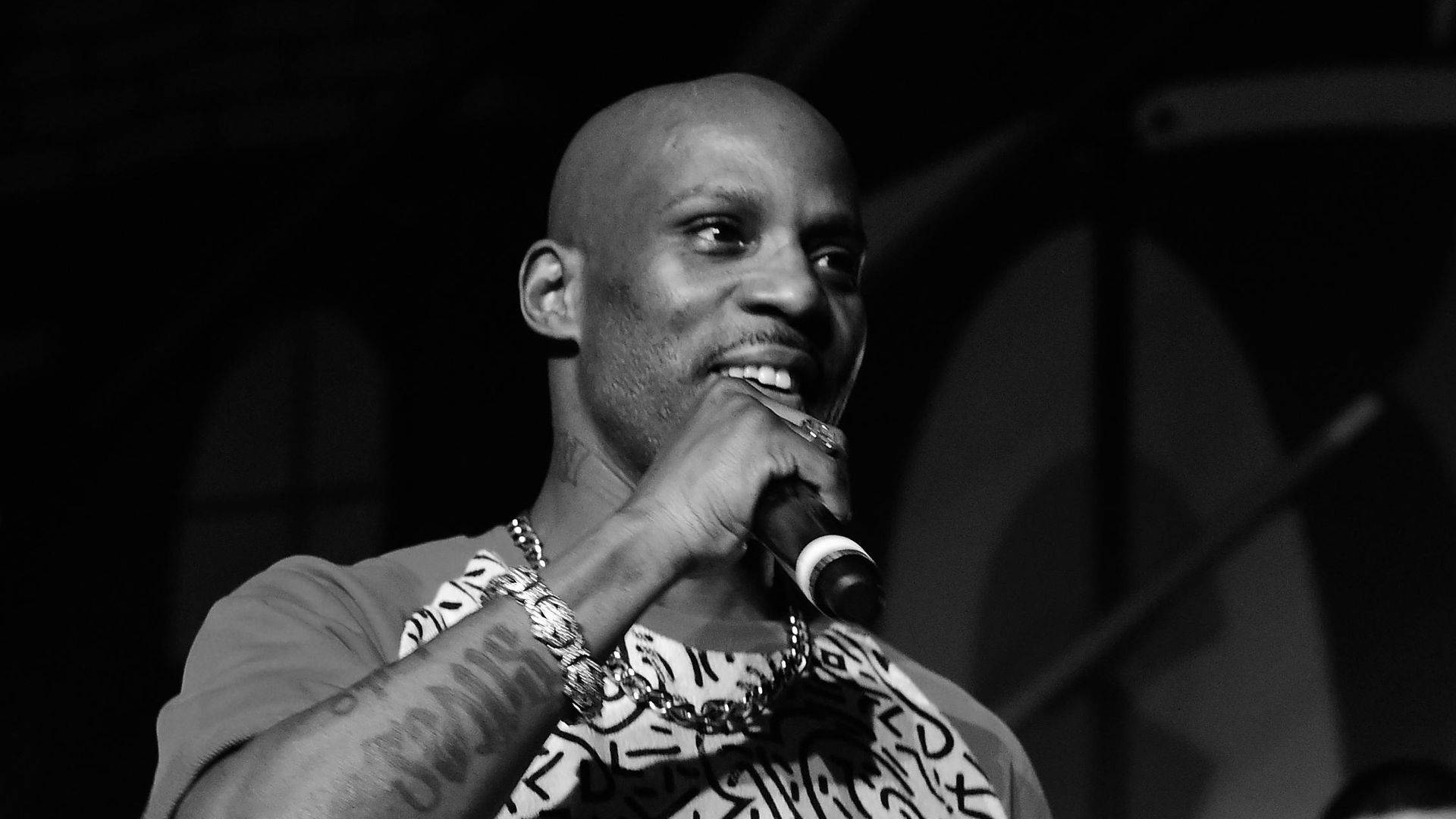 Dmx 桌布 壁紙 — 一個光頭紋身男子在昏暗的舞台場景中微笑著拿著麥克風。
