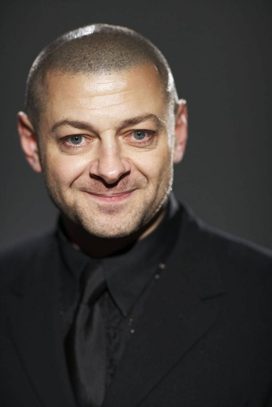 actor 桌布 壁紙 — 一個光頭藍眼男人穿著黑色西裝，在深灰色背景前溫暖微笑的特寫肖像。
