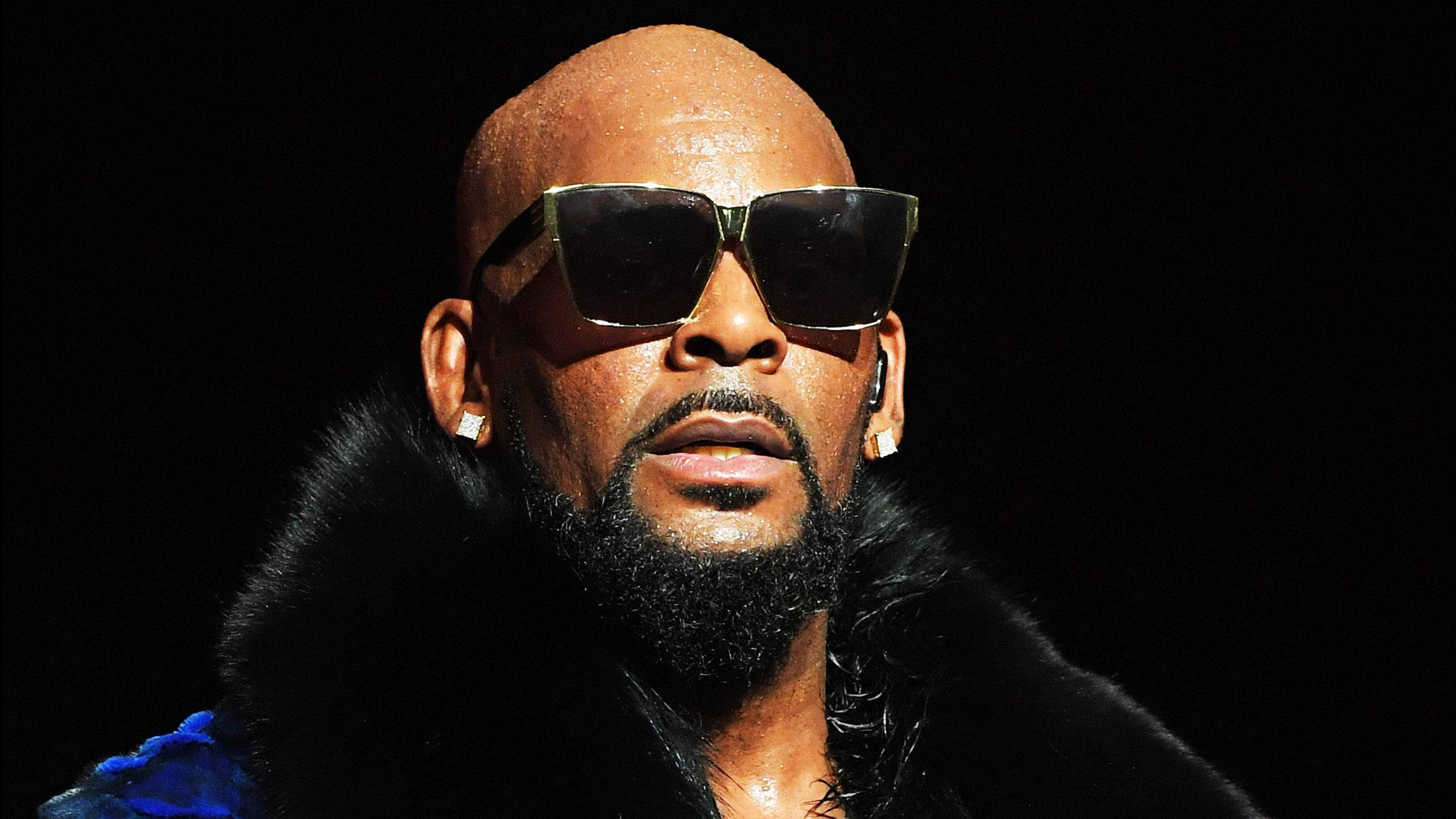 r kelly 桌布 壁紙 — 一個光頭鬍鬚男戴著超大太陽眼鏡和黑色毛領，背景深色。
