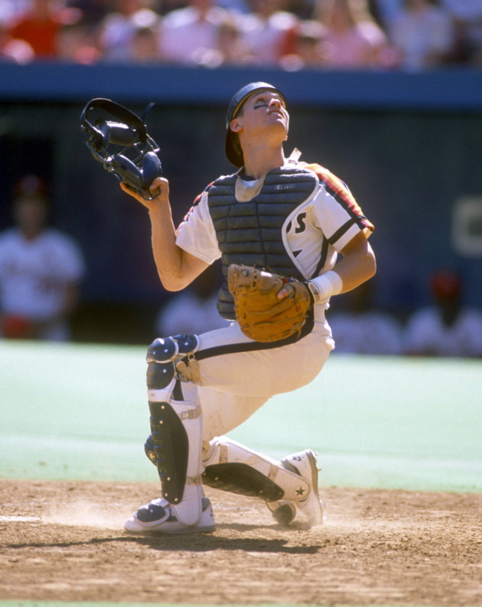 Craig Biggio 桌布 壁紙 — 一個全副裝備的棒球捕手蹲在泥地球場上，在明亮的日間比賽中仰望天空。