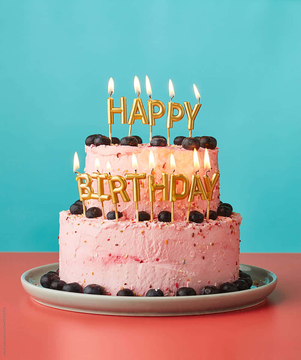 Happy Birthday Cake 桌布 壁紙 — 一個兩層粉紅色生日蛋糕，飾有金色「生日快樂」蠟燭和新鮮藍莓，背景為充滿活力的藍綠色。