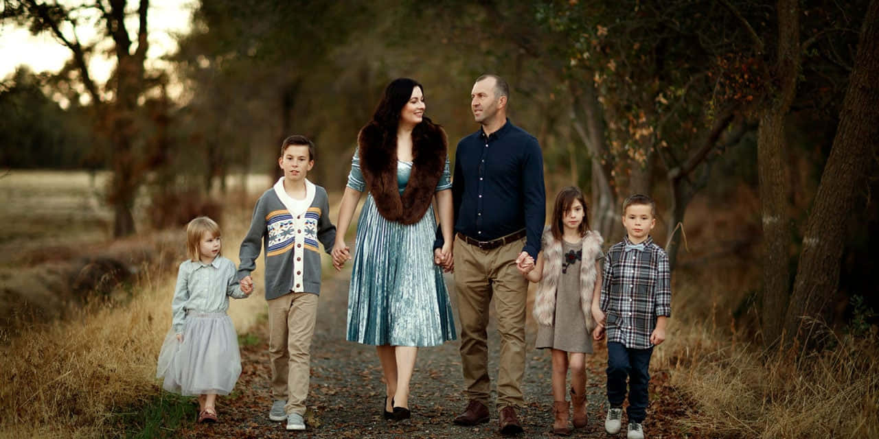 Family 桌布 壁紙 — 一個六人家庭在黃金時段手牽手走在樹木成蔭的泥濘小徑上，伴隨著溫暖的秋日色調。