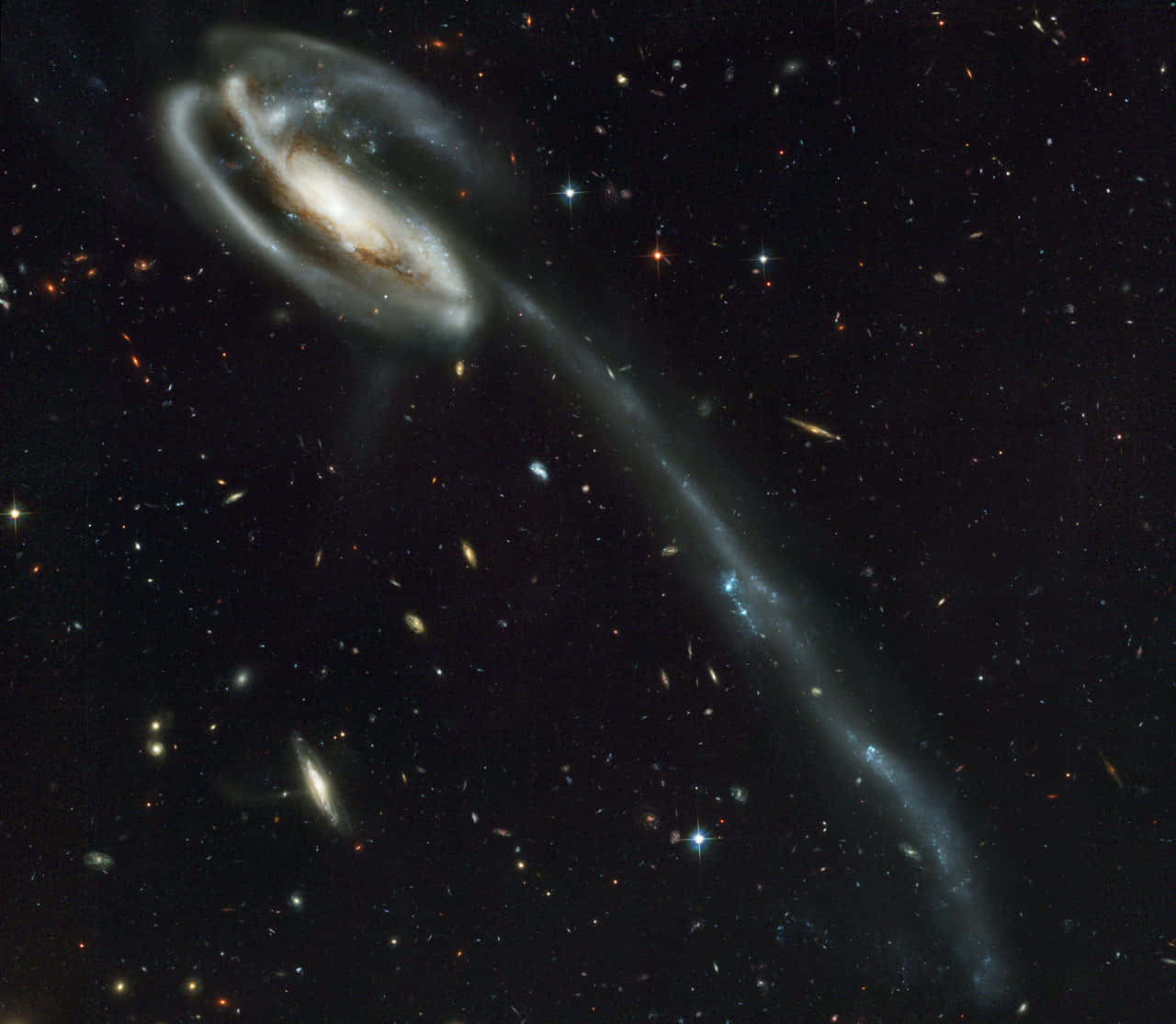 Nasa Galaxy 桌布 壁紙 — 一個具有明亮核心和旋轉臂的螺旋星系，在星場背景下與一條長潮汐尾相撞。