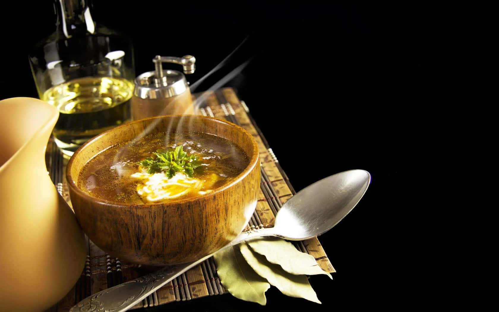 Winter Food 桌布 壁紙 — 一個冒煙的木碗，盛載著以香草和奶油裝飾的濃郁湯底，放在竹蓆上，旁邊有湯匙和橄欖油瓶，背景為黑色。