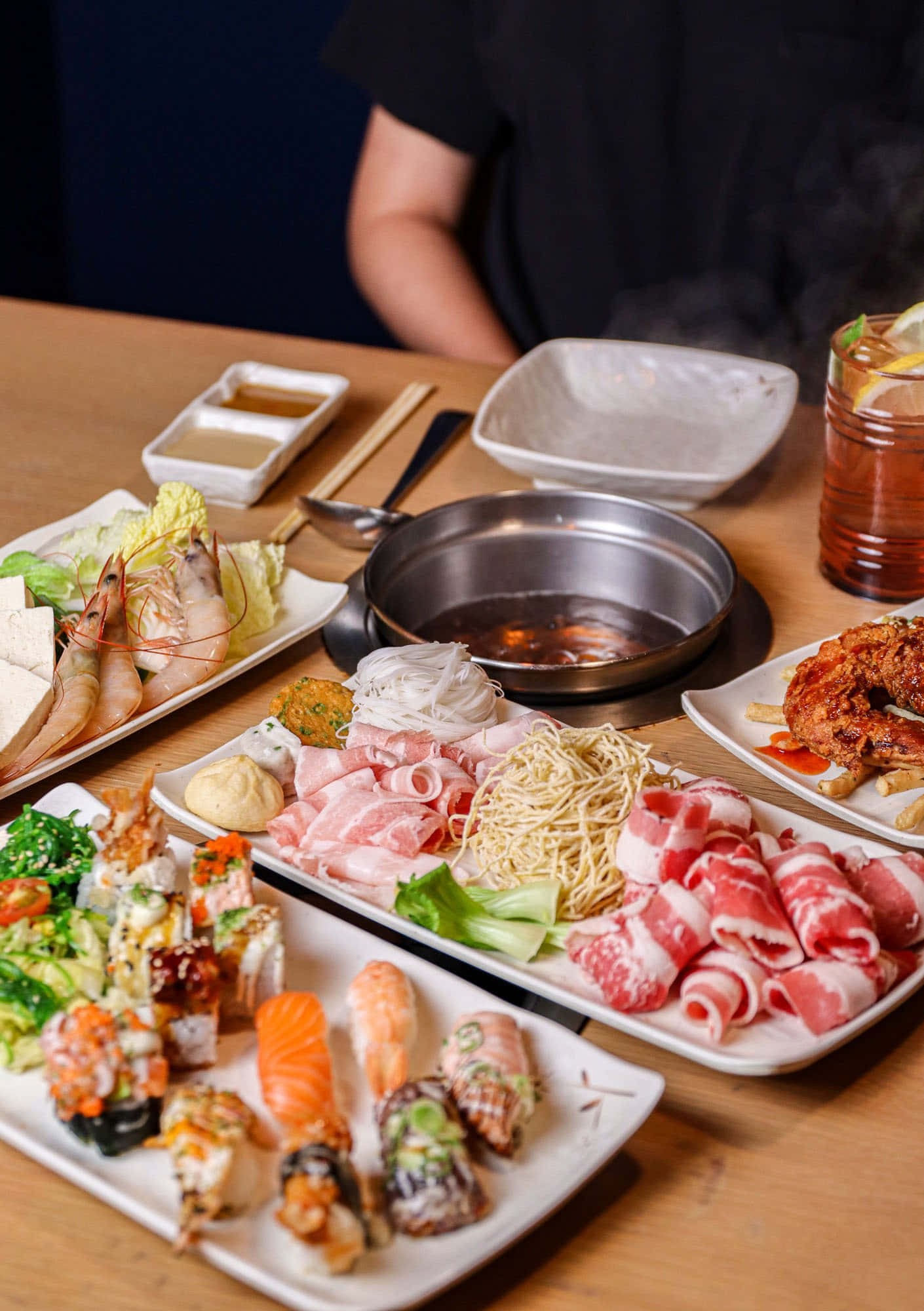 meat 桌布 壁紙 — 一個冒煙的熱鍋，周圍放著壽司、刺身、生牛肉卷和蝦的盤子，在木桌上。