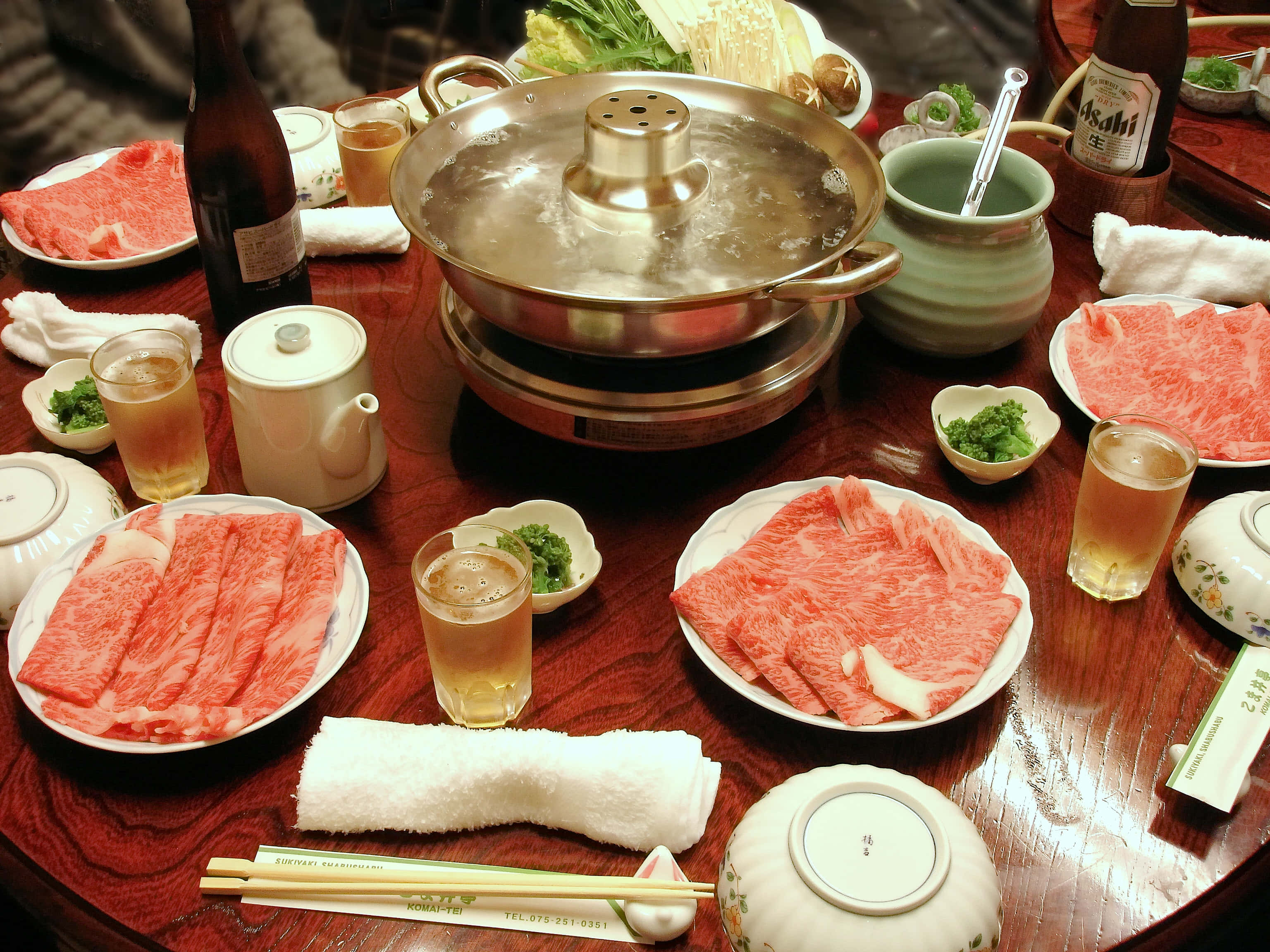meat 桌布 壁紙 — 一個冒煙的熱鍋，周圍放著幾碟生牛肉片和飲料，放在木桌上。