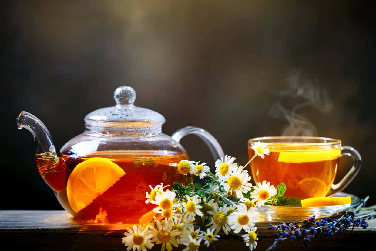 Morning Tea 桌布 壁紙 — 一個冒煙的玻璃茶壺和杯子，裝滿琥珀色茶，飾以柳橙片和雛菊，放在鄉村風木桌上。
