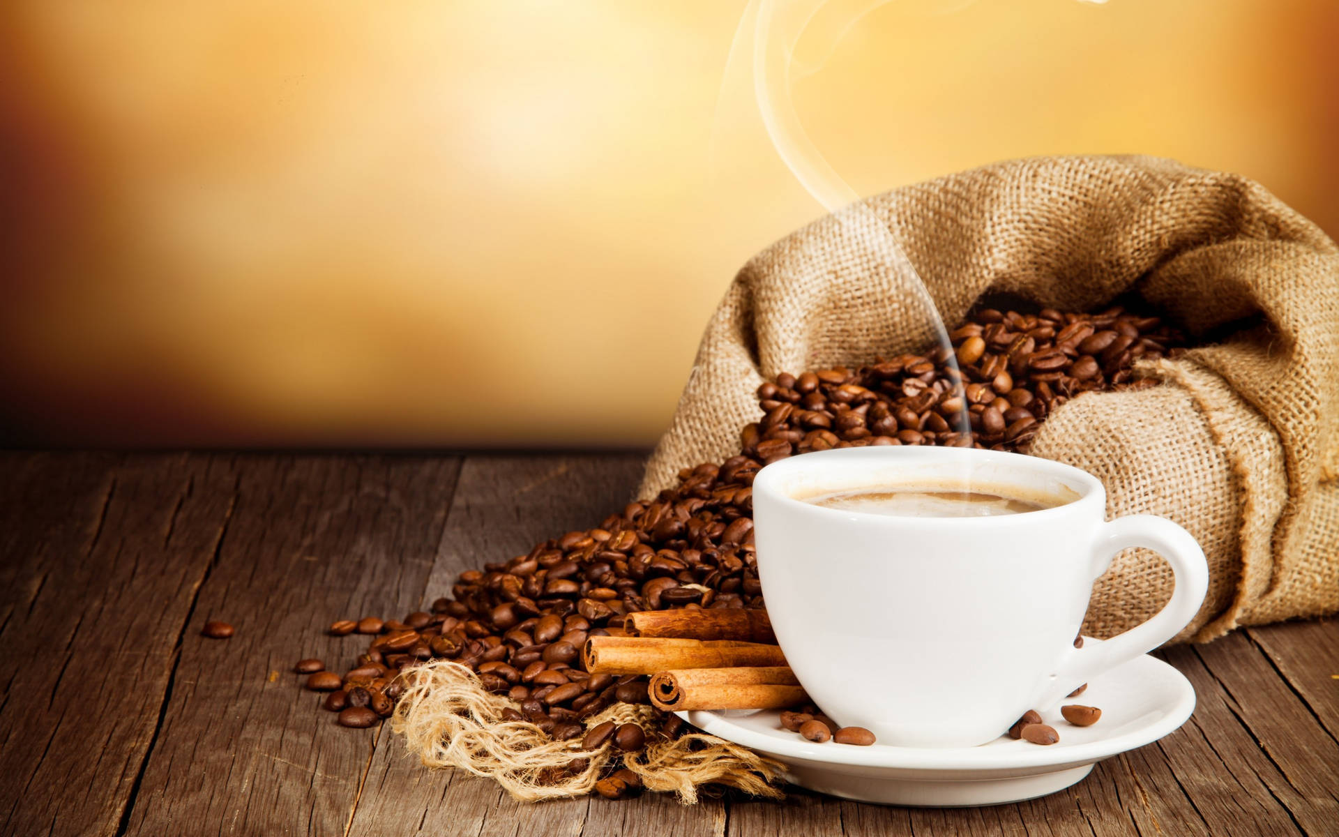Coffee Bean 桌布 壁紙 — 一個冒煙的白色咖啡杯放在一個麻布袋旁邊，麻布袋裡灑出烘焙過的咖啡豆和肉桂棒在質樸的木桌上。