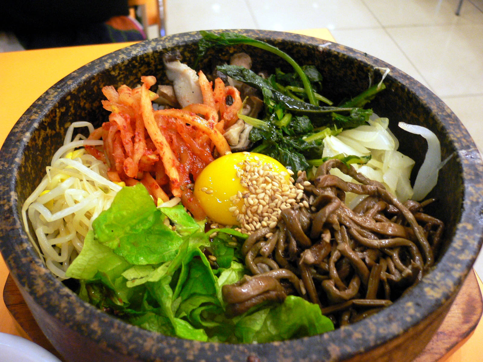 烹飪 桌布 壁紙 — 一個冒煙的石鍋韓國拌飯，上面放著鮮豔的泡菜、生雞蛋、芝麻和新鮮蔬菜。