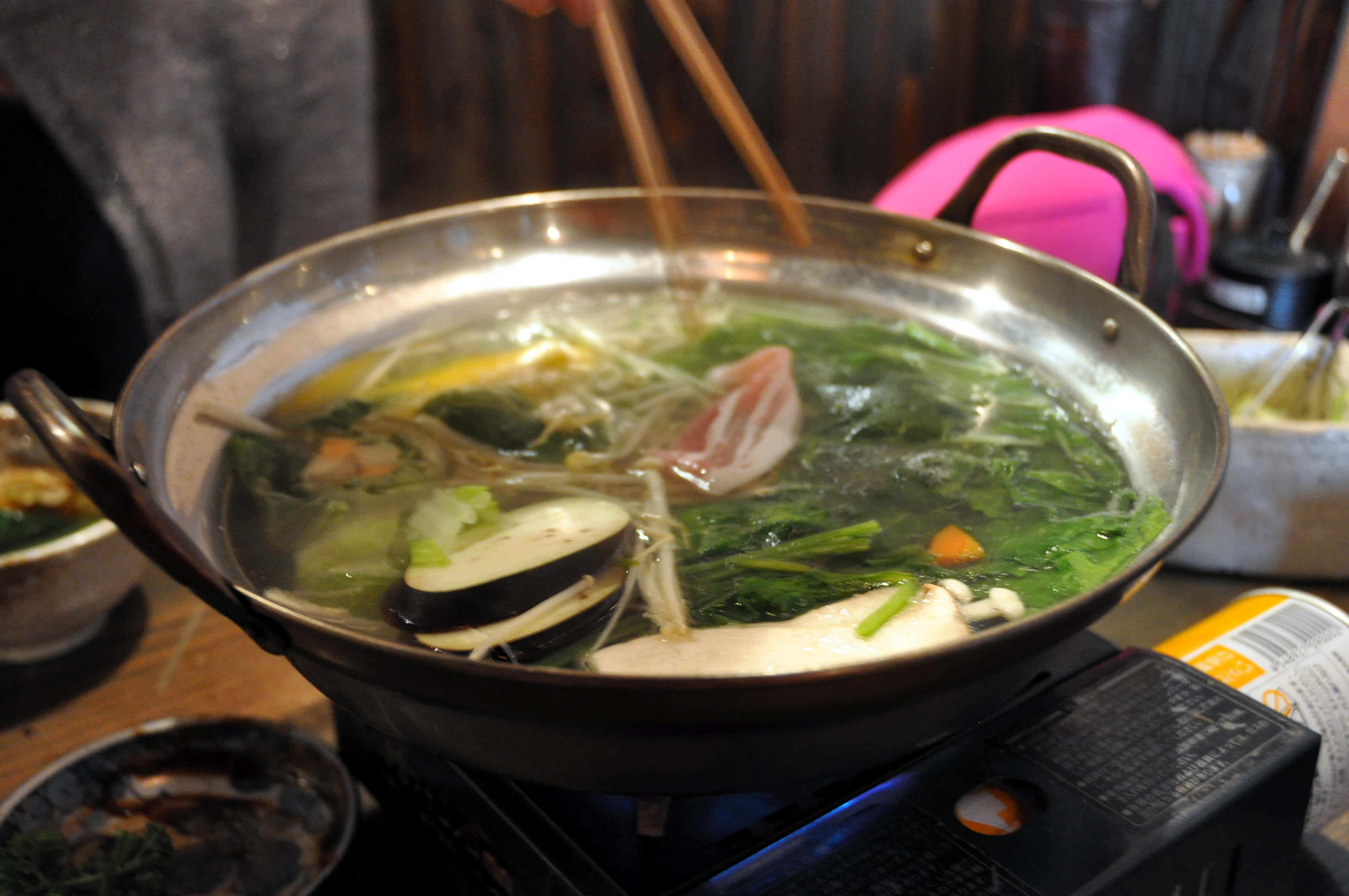 meat 桌布 壁紙 — 一個冒著熱氣的鍋，裡面燉著蔬菜、茄子和肉，筷子從湯汁中夾起一片培根。