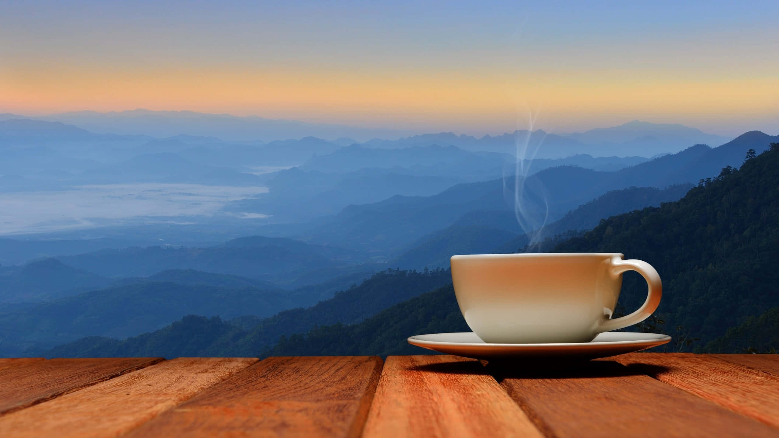 Coffee Aesthetic 桌布 壁紙 — 一個冒著蒸氣的白咖啡杯放在木桌上，俯瞰著日出時霧氣繚繞的山脈。