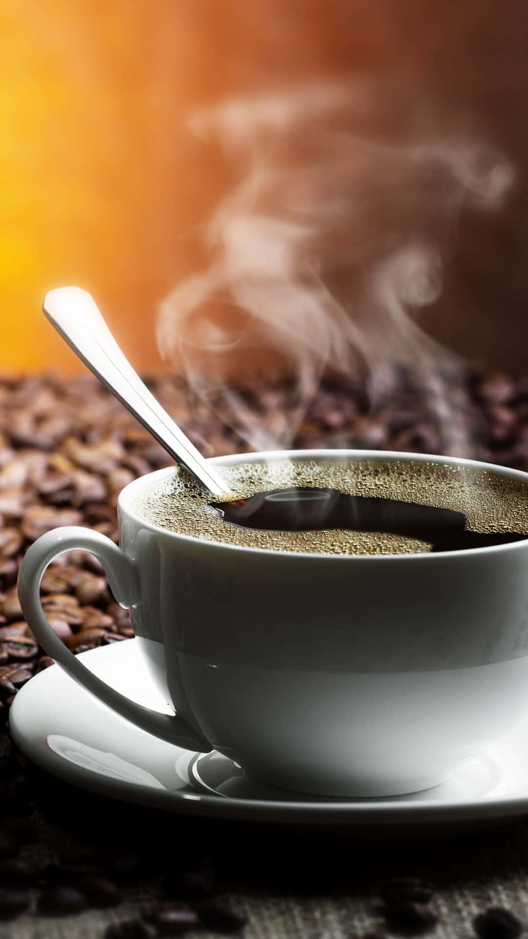 Coffee Aesthetic 桌布 壁紙 — 一個冒著蒸氣的白色咖啡杯連湯匙放在碟子上，周圍環繞著咖啡豆，沐浴在溫暖的金色光線下。