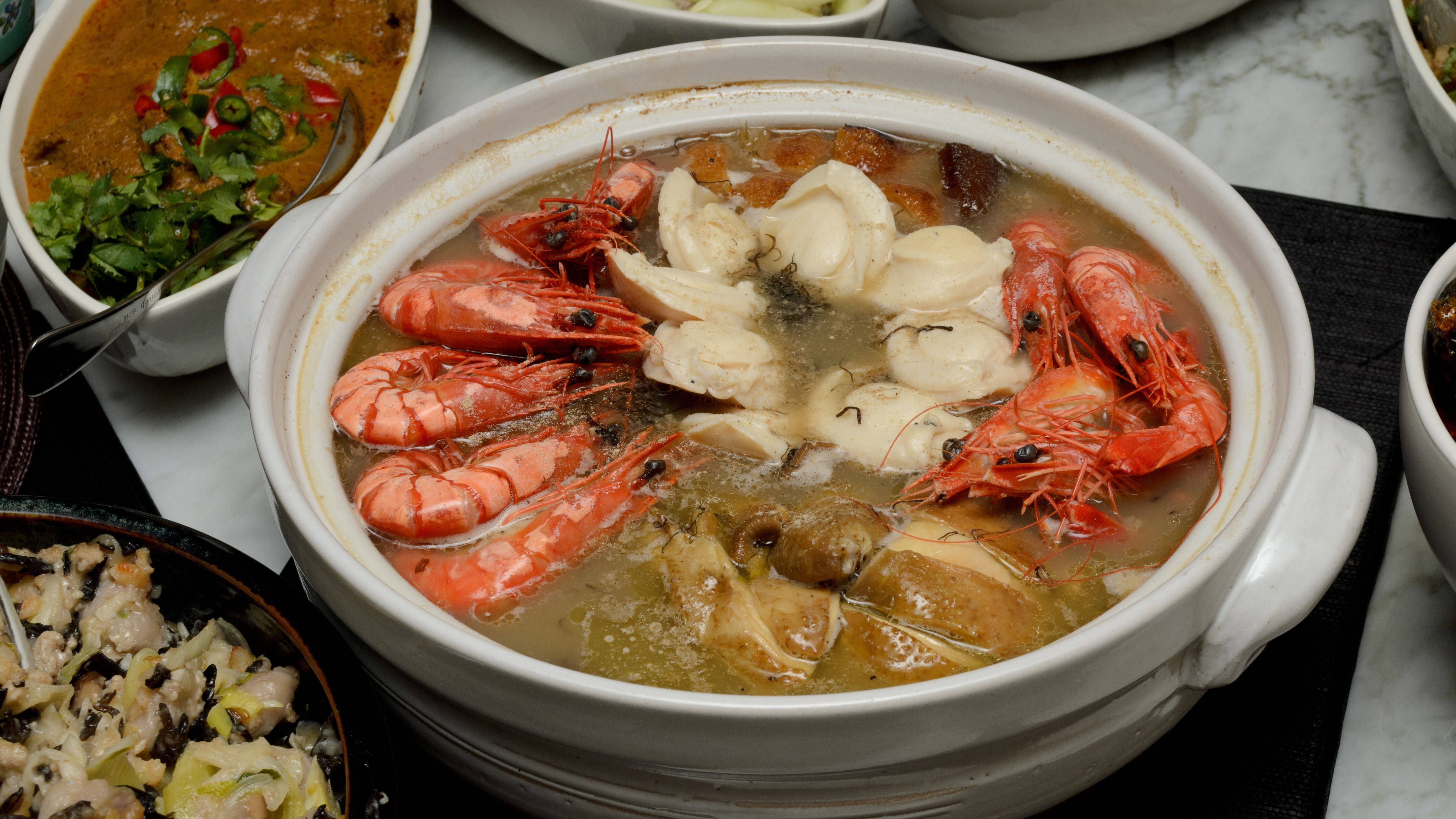 Seafood 桌布 壁紙 — 一個冒著蒸氣的白陶鍋，盛滿鮮豔的粉紅蝦、扇貝和蘑菇，在濃郁的湯汁中，周圍環繞著配菜。