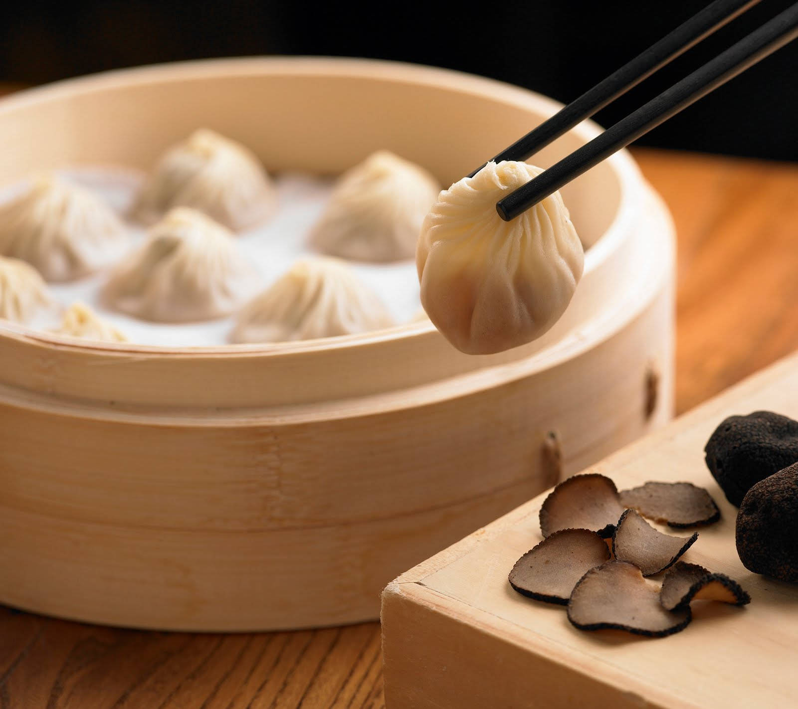 steam 桌布 壁紙 — 一個冒著蒸氣的竹籠盛著精緻的點心，筷子夾起一個，旁邊放著切片松露。