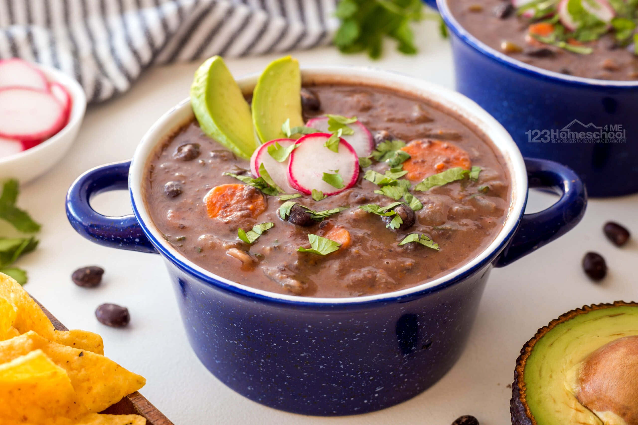 Black Bean Soup 桌布 壁紙 — 一個冒著蒸氣的藍色琺瑯碗，盛滿濃郁的黑豆湯，上面放著酪梨片、蘿蔔片和新鮮香菜。