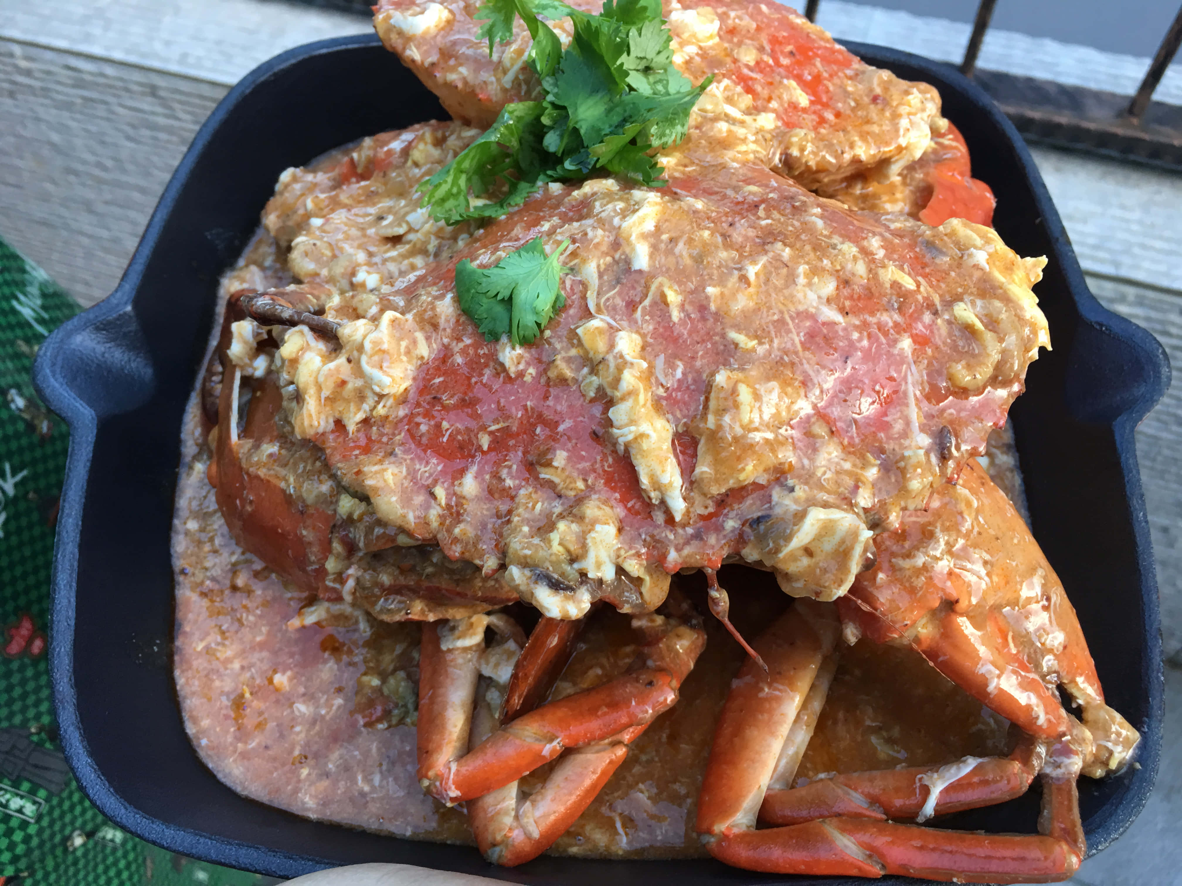 Crab 桌布 壁紙 — 一個冒著蒸氣的鑄鐵鍋，堆滿了多汁的蟹腿和蟹肉塊，配上濃郁的醬汁，並用新鮮的香菜點綴。