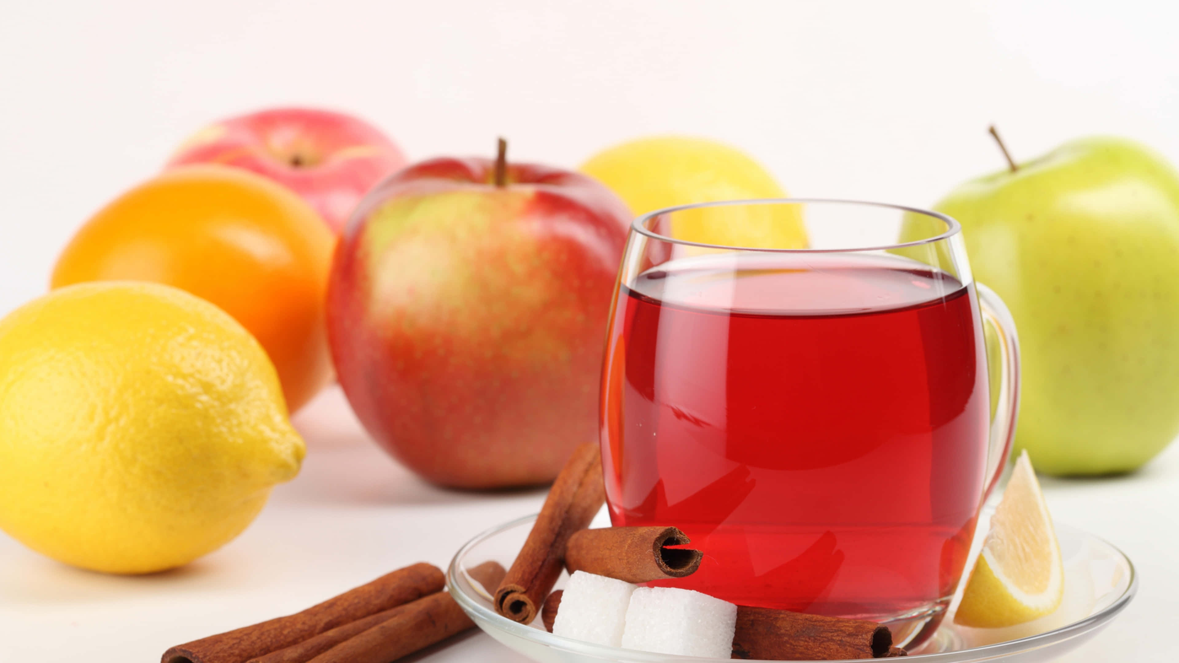 Food And Beverage 桌布 壁紙 — 一個冒著蒸氣的香料紅茶馬克杯，周圍是新鮮蘋果、檸檬和肉桂棒，放在乾淨的白色表面上。