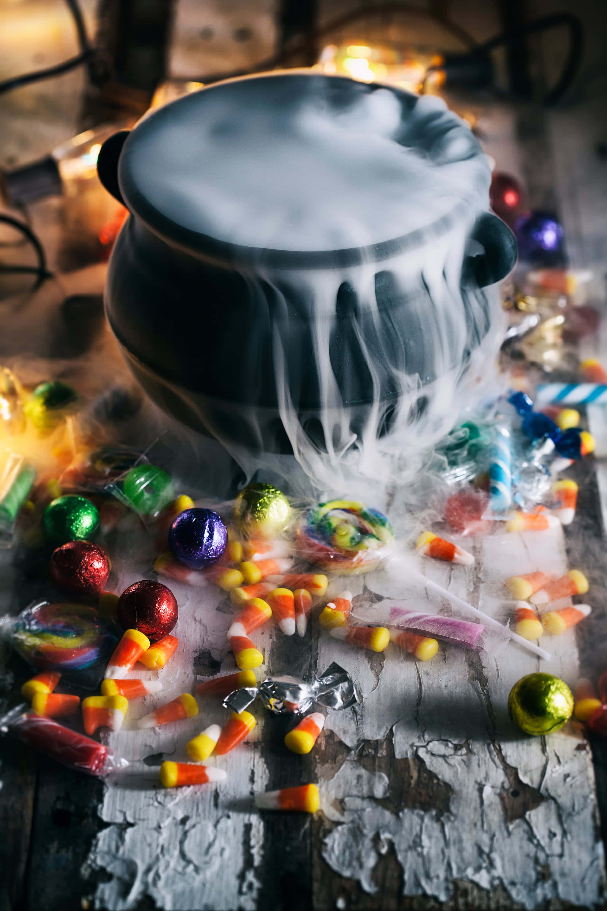 cauldron 桌布 壁紙 — 一個冒著蒸氣的黑鍋放在質樸的木桌上，將詭異的白色蒸氣灑在散落的萬聖節糖果上。