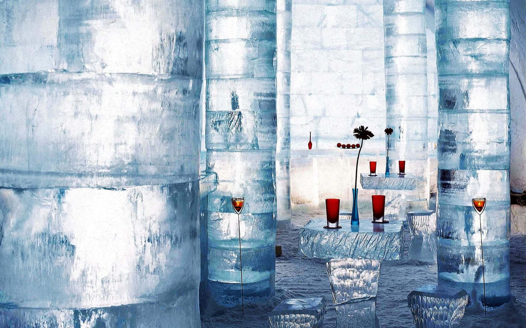 Ice Hotel 桌布 壁紙 — 一個冰冷的冰吧，高聳的半透明柱子和紅色玻璃杯在冷藍色調中閃耀。