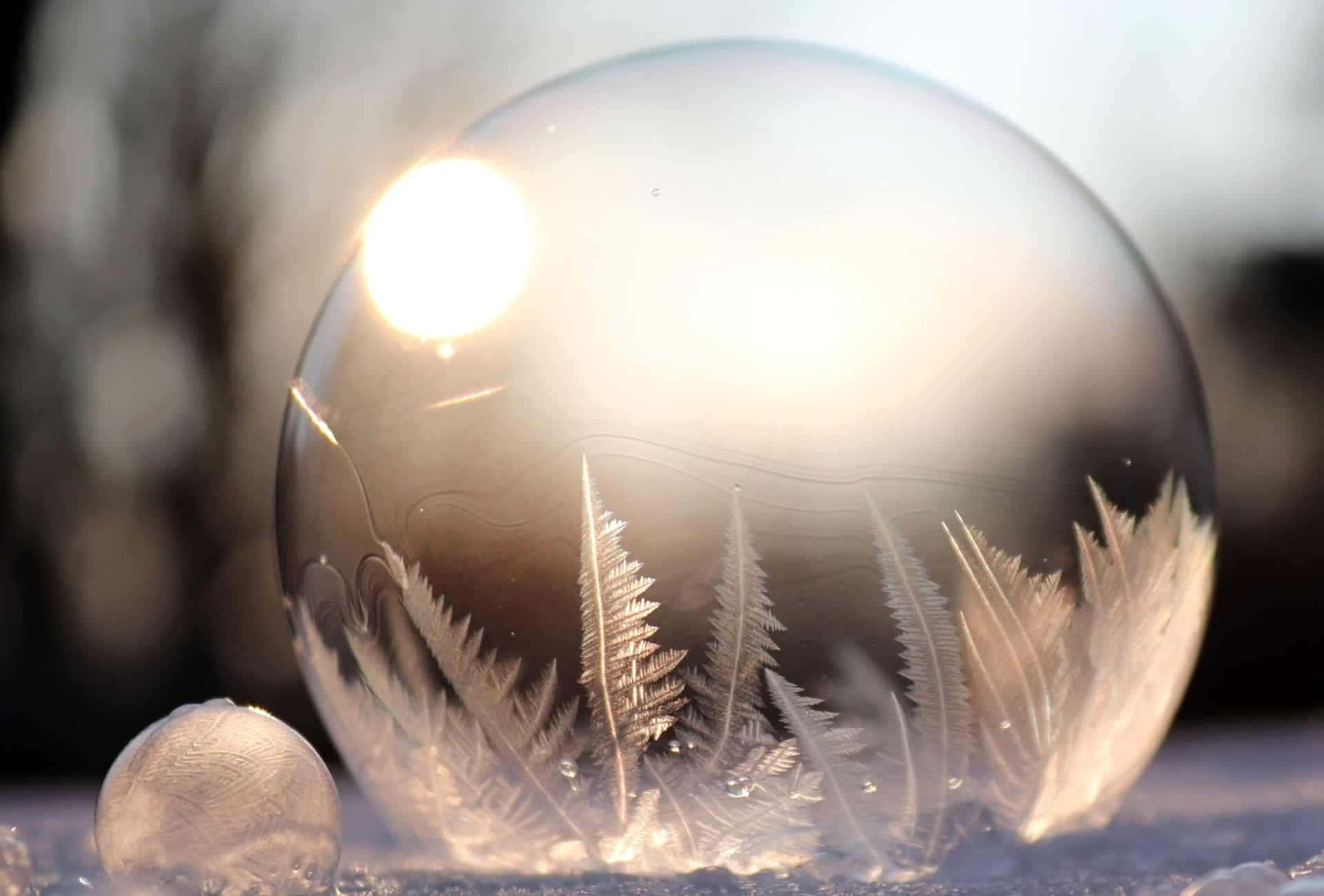 Bubbles 桌布 壁紙 — 一個冰凍的玻璃球體，裡面有精緻的霜蕨，在白雪皚皚的冬季背景下反射出明亮的太陽。