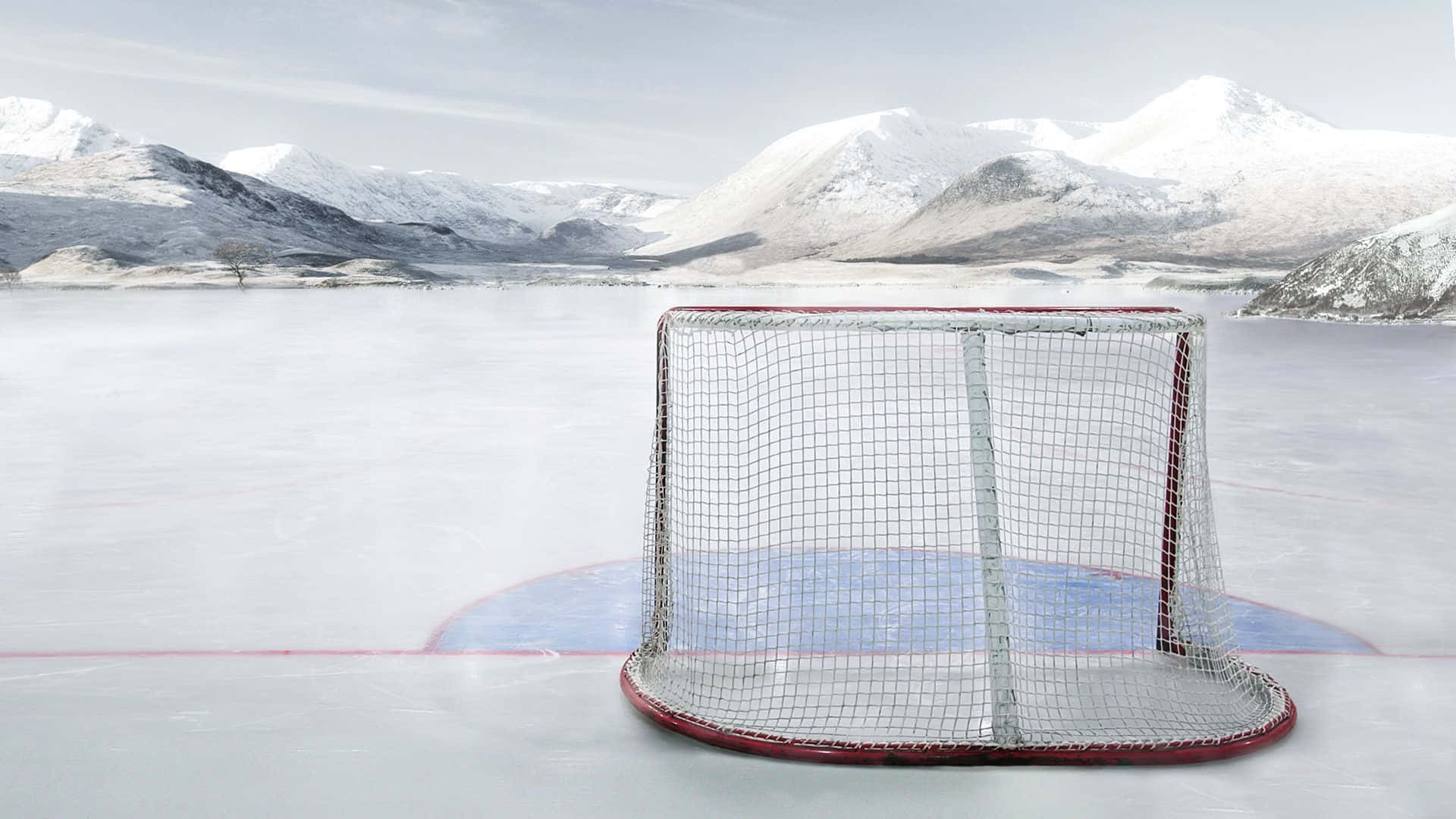 hockey 桌布 壁紙 — 一個冰球球門矗立在冰凍的湖面上，四周被白雪覆蓋的山脈環繞，天空蒼白。