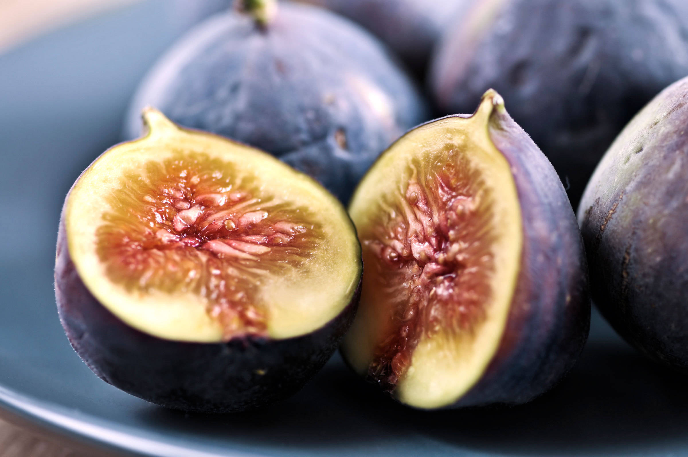 Fruits 桌布 壁紙 — 一個切開的無花果的特寫，在深藍色盤子上露出多汁的粉紅色和黃色內部。