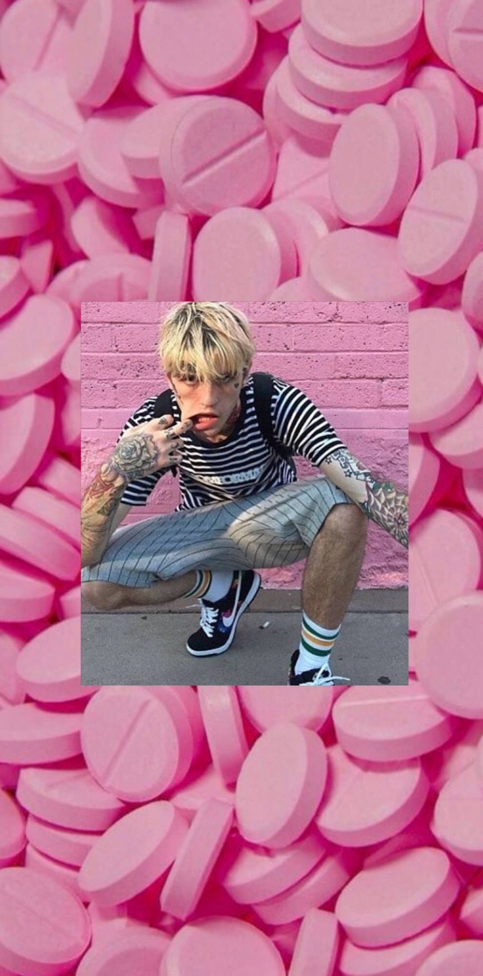 Peep 桌布 壁紙 — 一個刺青年輕男子蹲在粉紅磚牆前，周圍是粉紅藥丸的海洋。