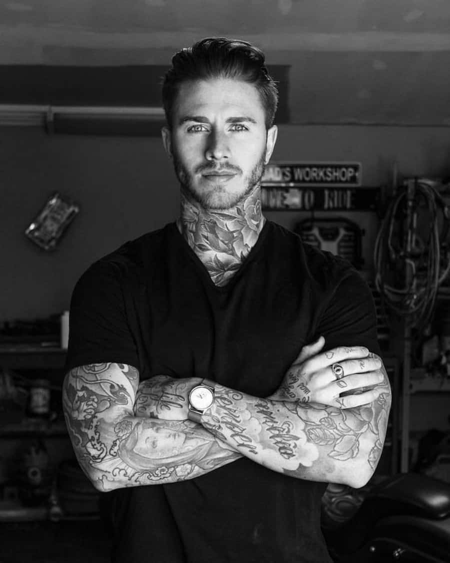Tattoo Boy 桌布 壁紙 — 一個刺青男子交叉雙臂自信地站在工作室裡，他的脖子和手臂上佈滿了複雜的黑白墨水圖案。