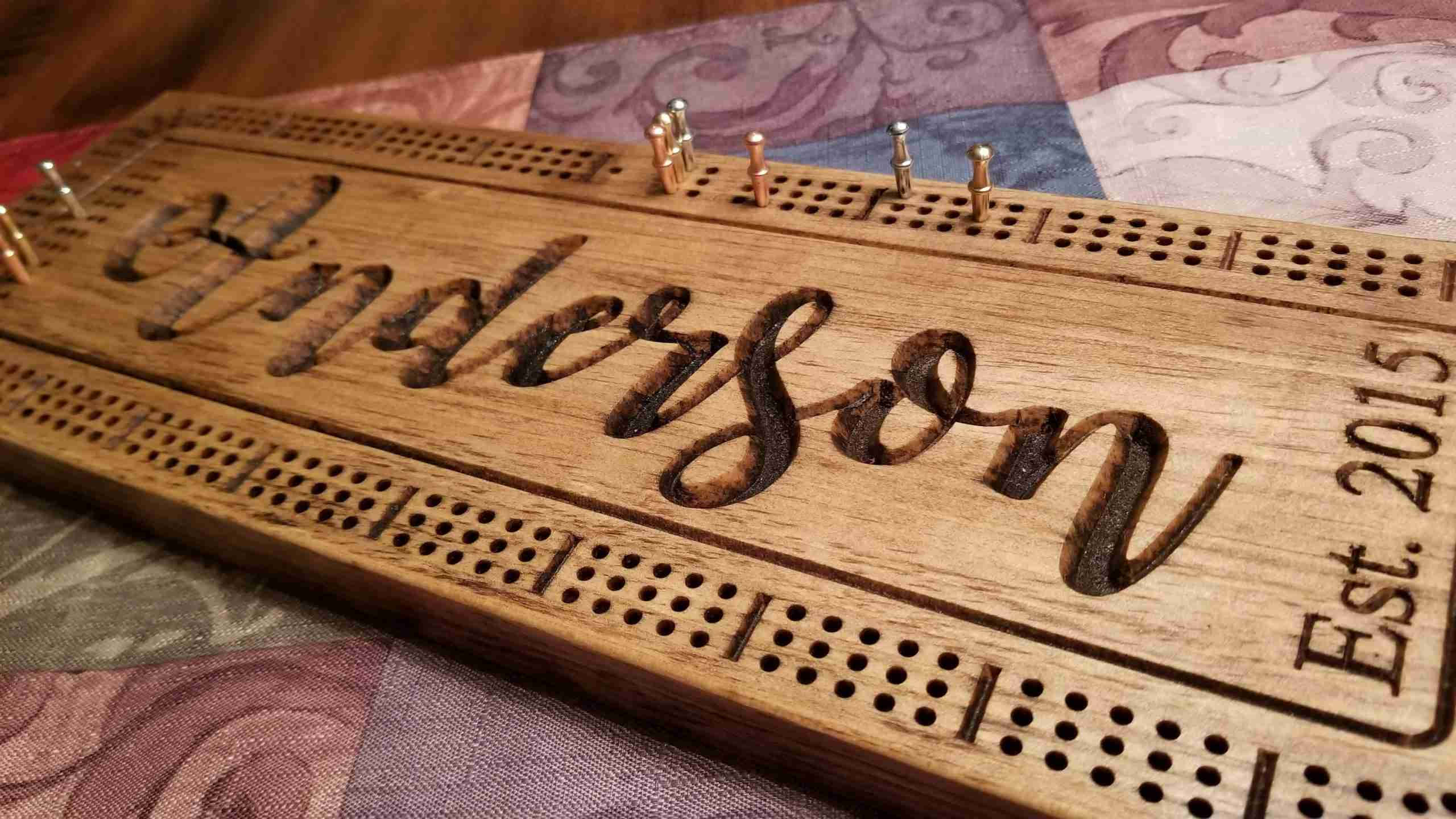 Board Game 桌布 壁紙 — 一個刻有「Anderson Est. 2015」的個人化木製克里比奇棋盤，放置在圖案織物表面上。