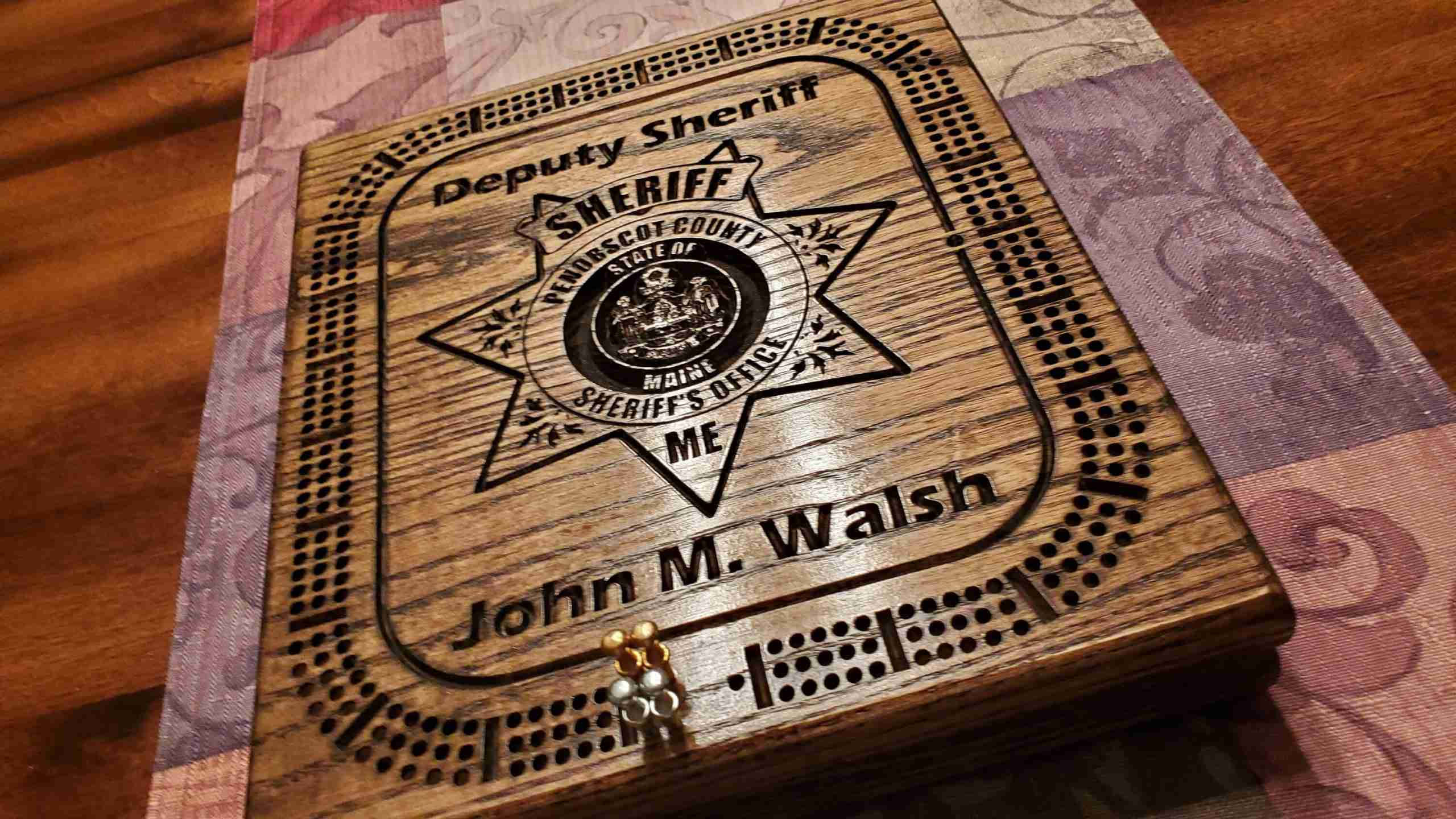Board Game 桌布 壁紙 — 一個刻有副警長星章和名字 John M Walsh 的木製餅乾盒，放在一塊有圖案的布上。
