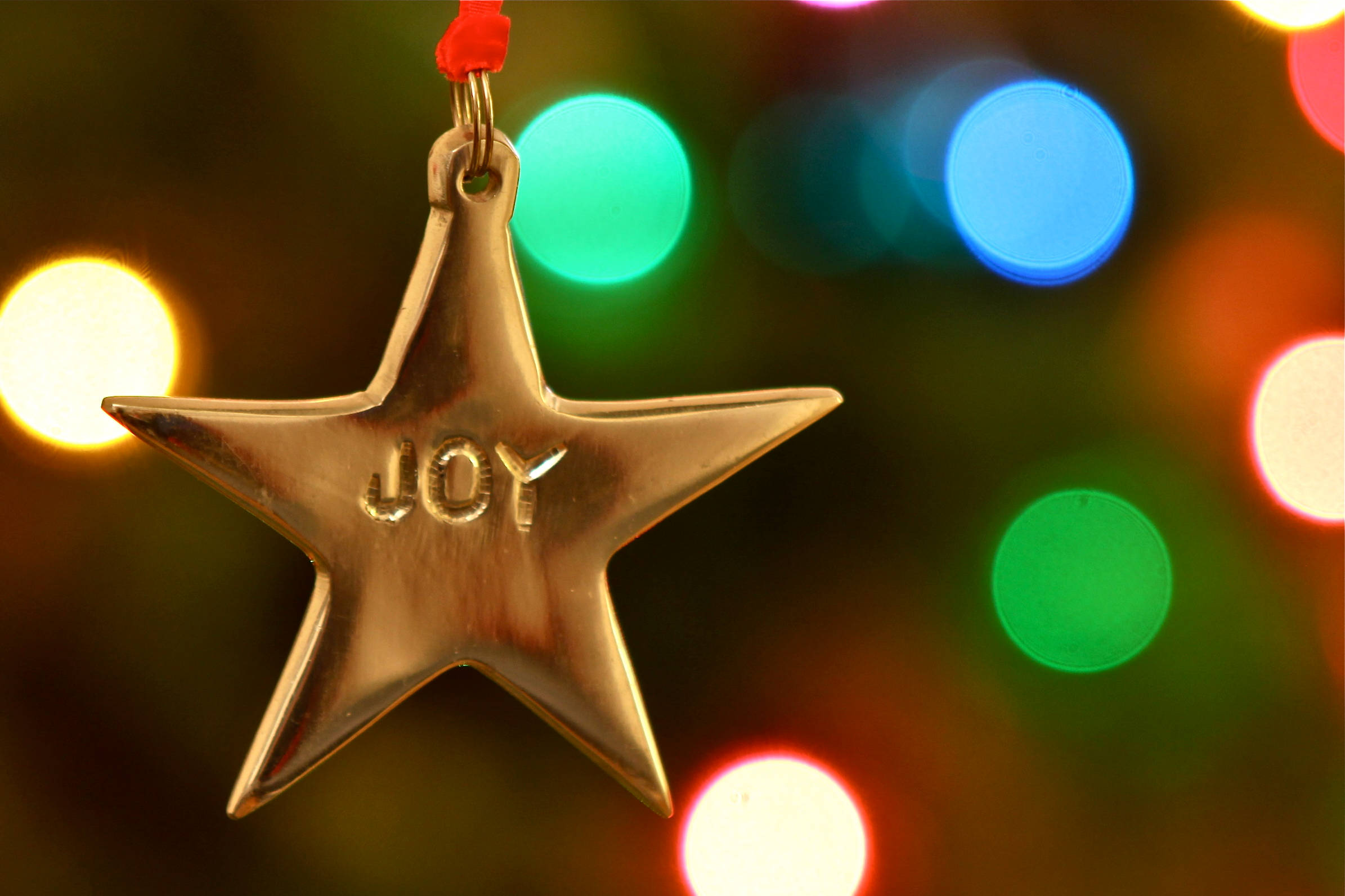 Joy 桌布 壁紙 — 一個刻有喜悅的金色星星裝飾，懸掛在充滿活力的節日燈光散景前。