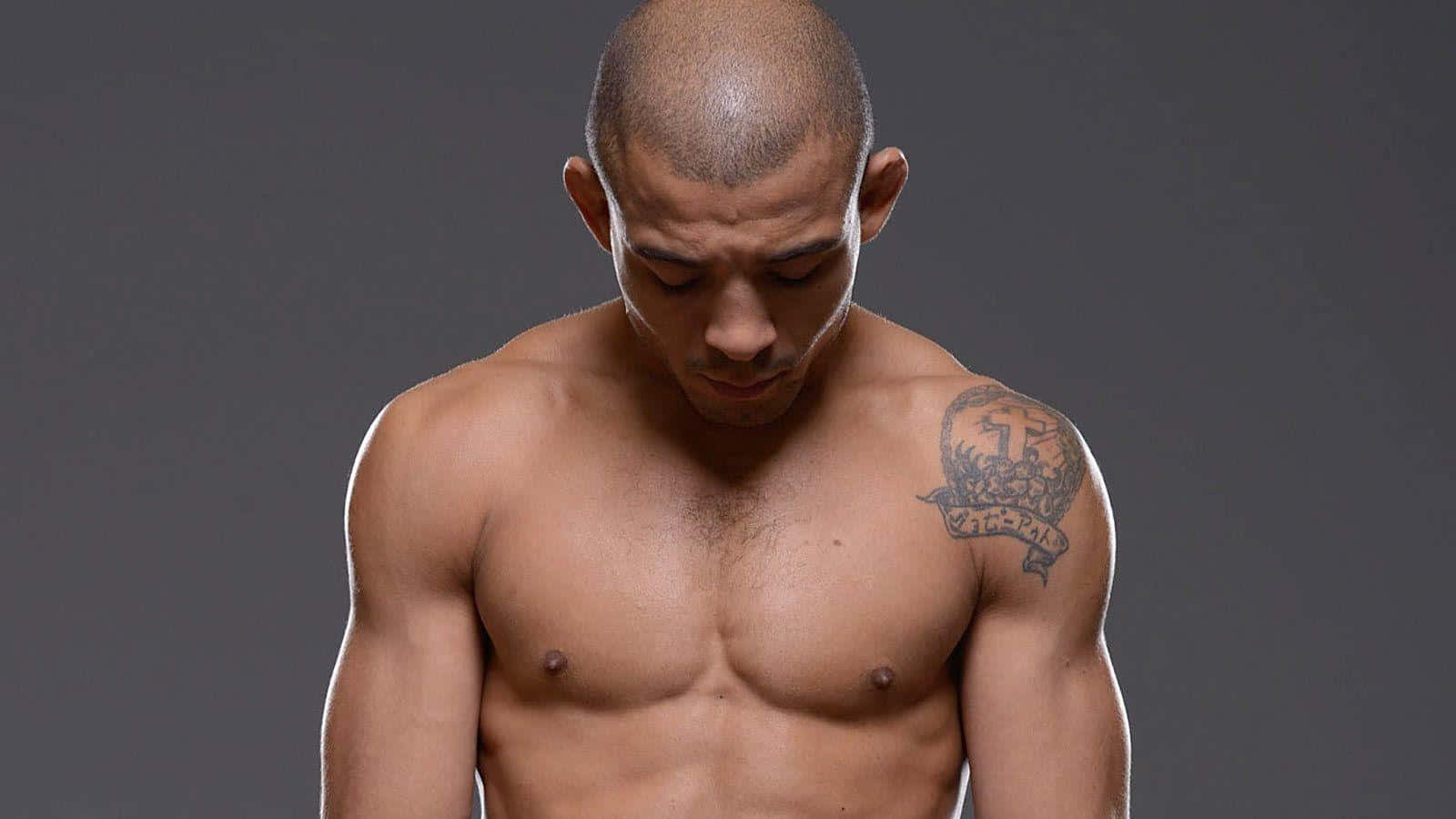 Athlete 桌布 壁紙 — 一個剃光頭、右肩有刺青的肌肉男，赤裸上身，在純灰色背景前向下看。