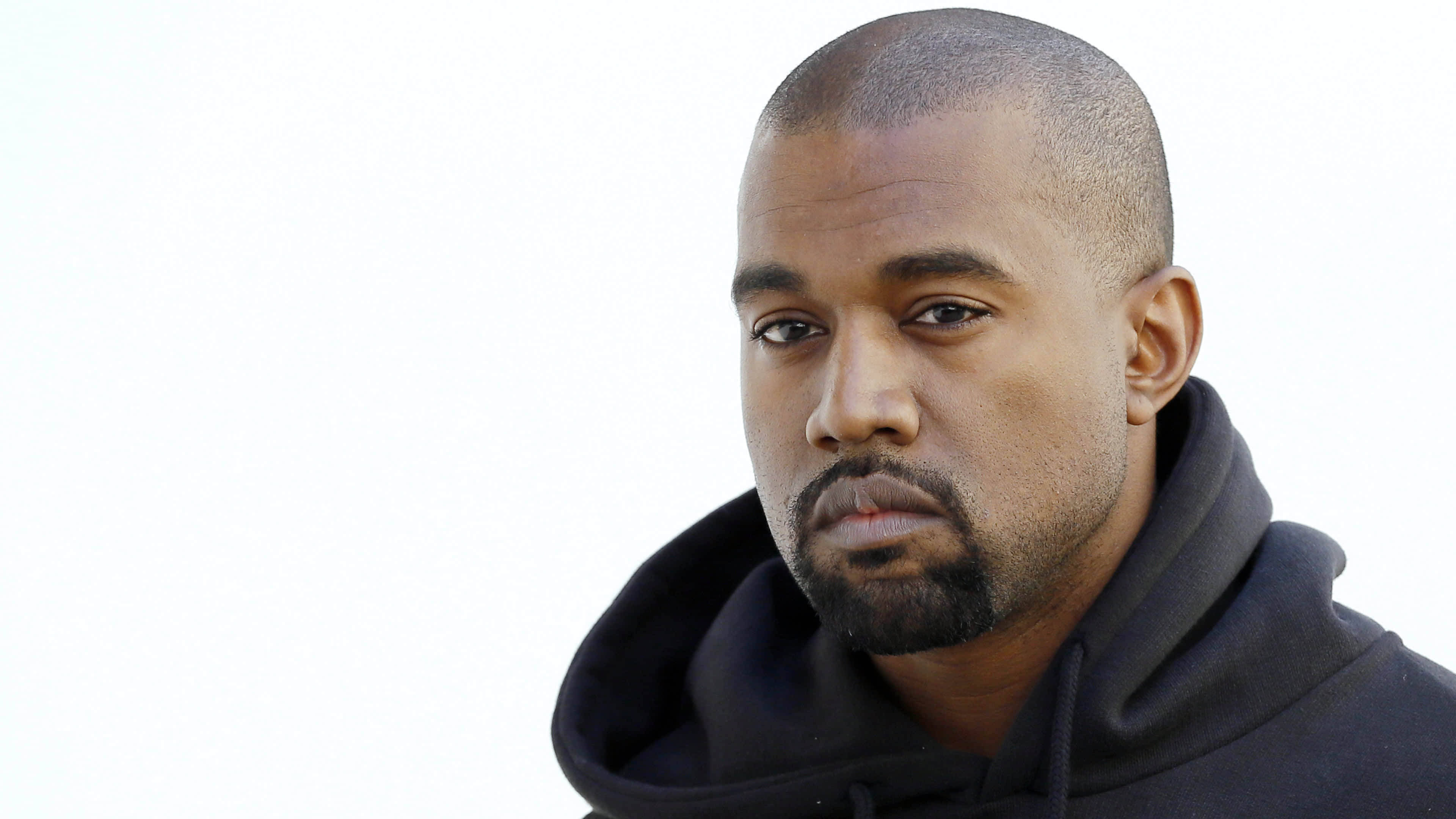 Kanye West 桌布 壁紙 — 一個剃光頭、留山羊鬍的男人穿著黑色連帽衫，在純白背景前的特寫肖像。