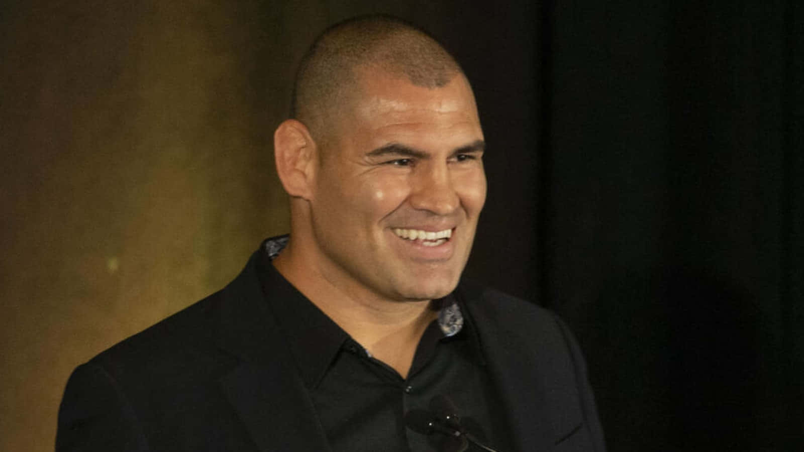 UFC 桌布 壁紙 — 一個剃光頭、穿黑色西裝和襯衫的男人在深色背景前微笑。