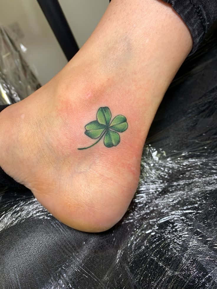 Four Leaf Clover 桌布 壁紙 — 一個剛紋好的四葉草紋身在黑色塑膠上的人腳上發出綠色光芒。