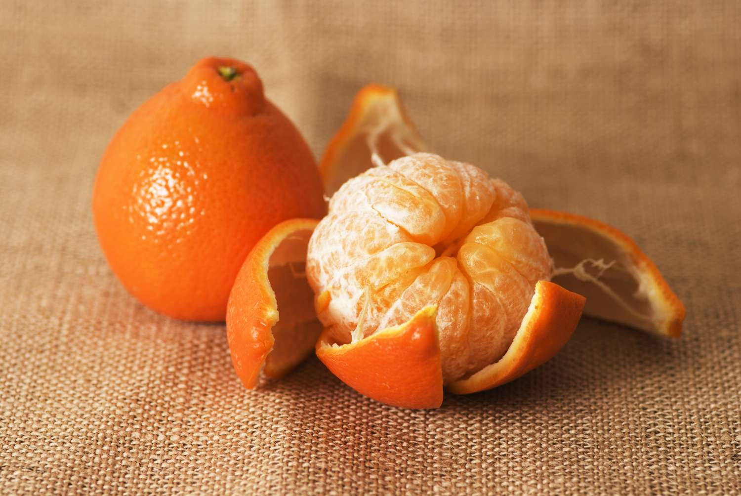 Fruits 桌布 壁紙 — 一個剝了皮的柑和一個完整的橙放在有紋理的粗麻布上，伴隨著溫暖的自然光線。