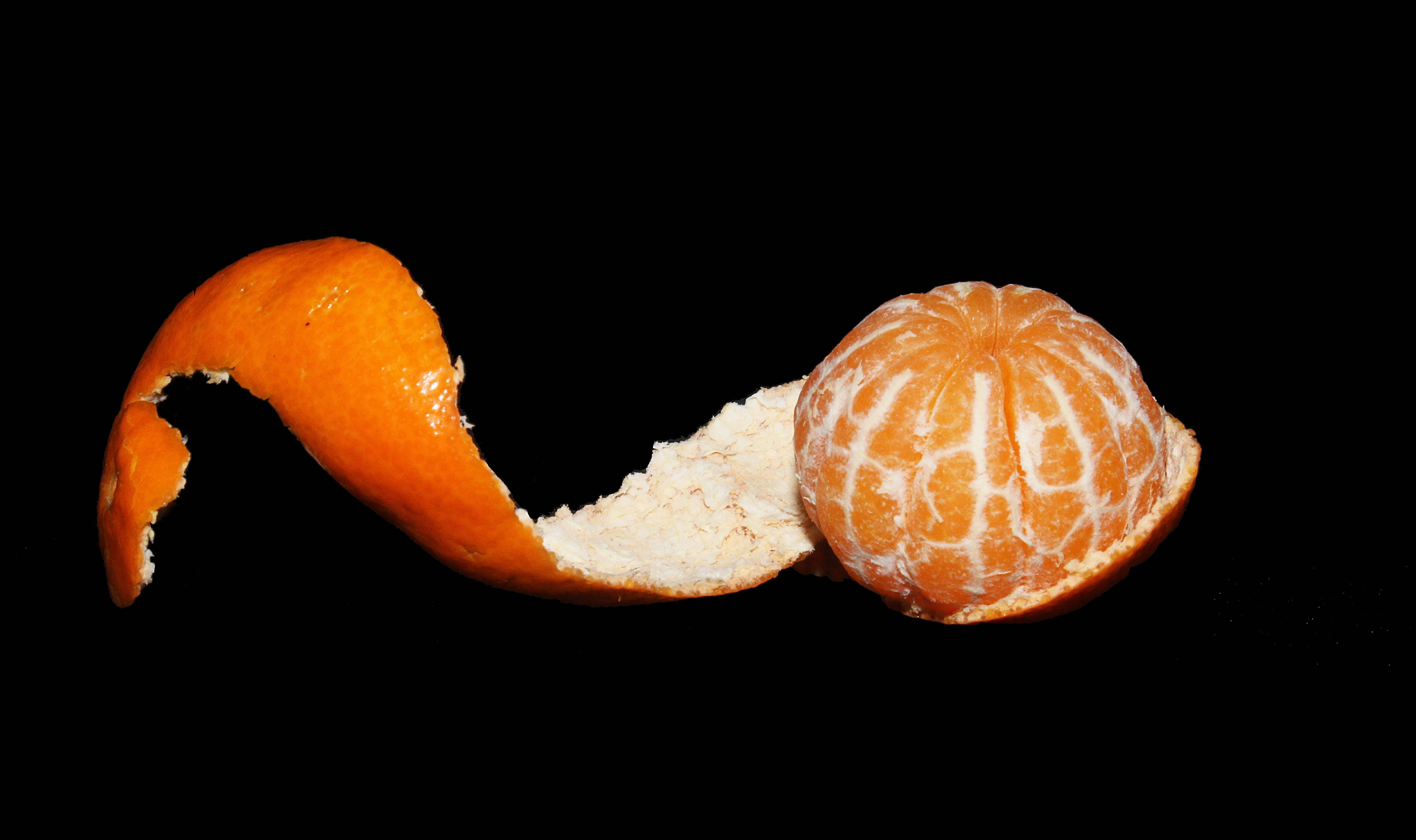 Fruit 桌布 壁紙 — 一個剝了皮的柑橘，其鮮豔的橙色果皮在純黑色背景下戲劇性地捲曲。
