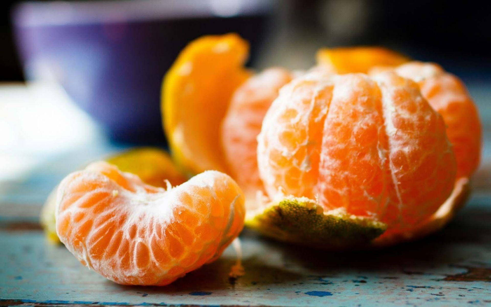 Fruit 桌布 壁紙 — 一個剝了皮的柑橘，多汁的瓣片放在經風化的藍色木質表面上，背景有一個模糊的紫色碗。