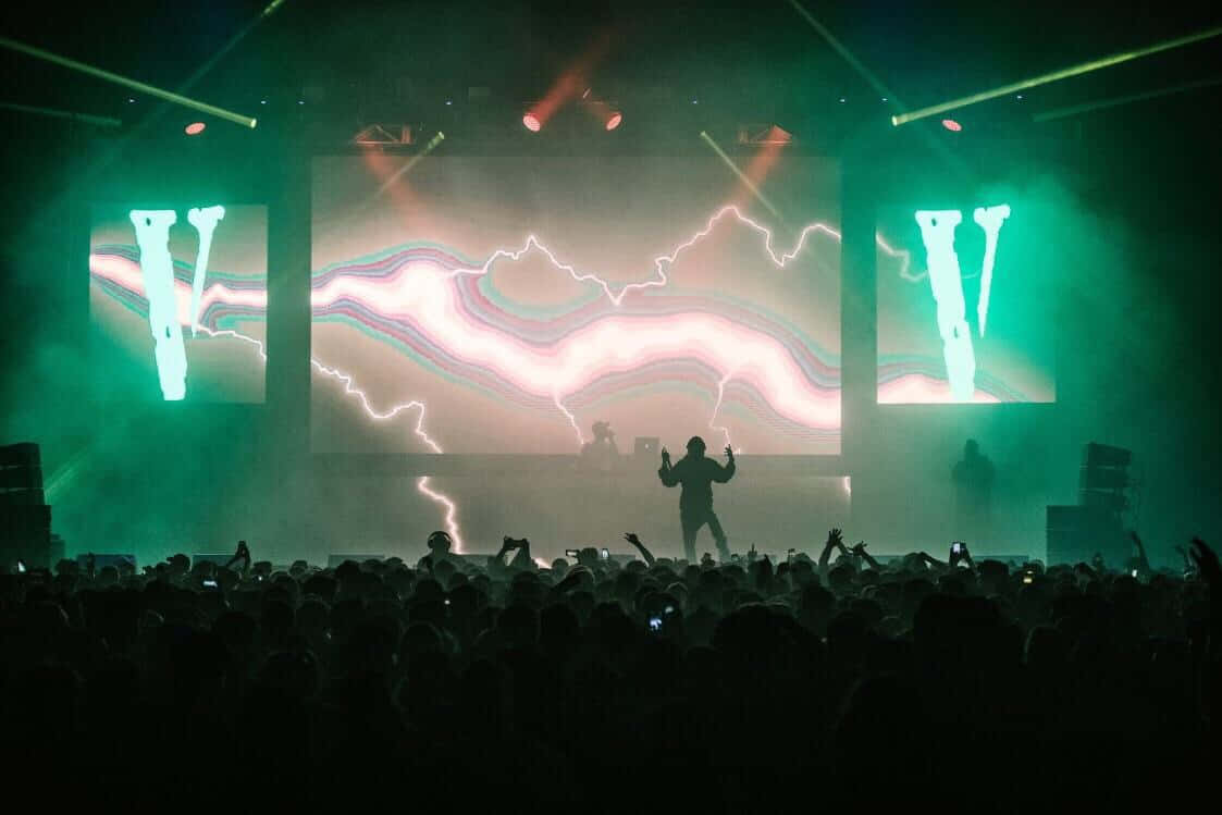 Playboi Carti 桌布 壁紙 — 一個剪影DJ在霓虹綠燈光和發光閃電主題背景下的擁擠音樂會人群中注入活力。